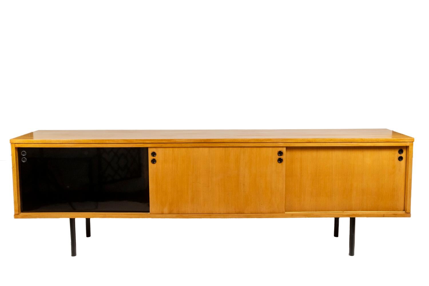 Joseph-André Motte, signed.

Sideboard in blond ash, opening on the front with three side doors, rectangular in shape with a central shelf in each part, resting on a black lacquered metal base. Round shaped handles.

French work realized in the