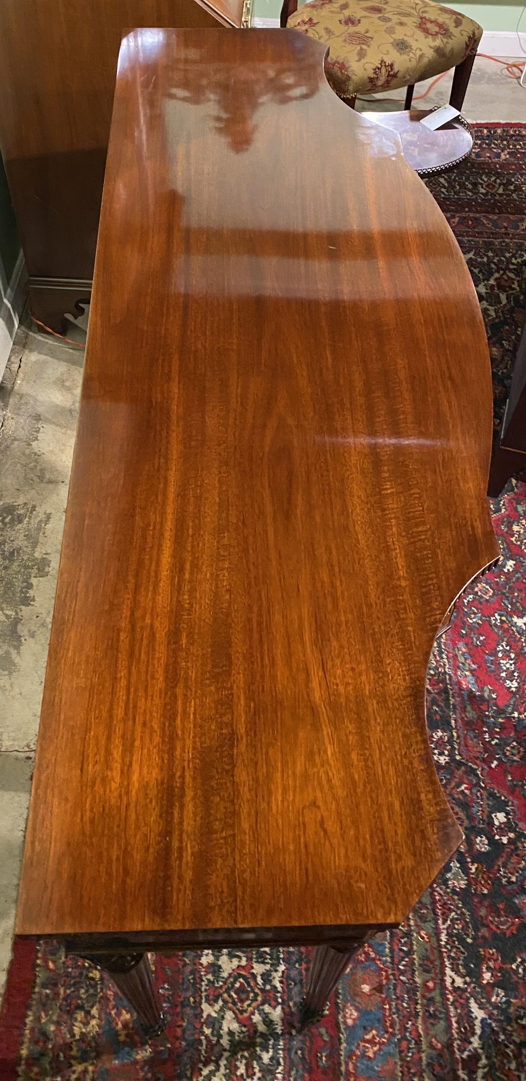 A finely carved custom mahogany console table from Joseph Gerte in Boston MA, with conforming shaped top surmounting a case three fitted frieze drawers with cross banded veneers and round punched brass pulls, the center of which is fitted for silver