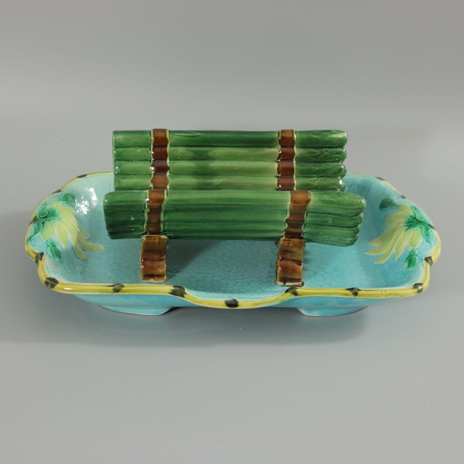 Holdcroft Majolica asparagus drainer which features asparagus tips bound together, sat on a rectangular tray. The tray with floral handles. Coloration: turquoise, green, brown, are predominant.