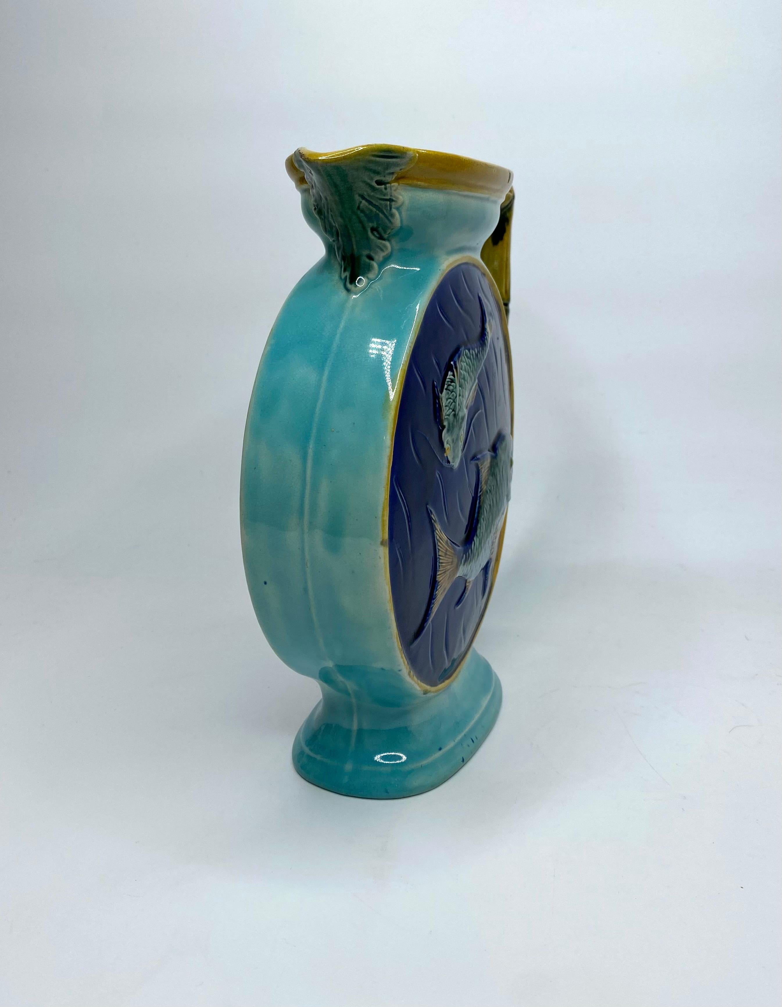 Joseph Holdcroft pottery majolica jug, c. 1870. The Japanesque style, circular jug, moulded to both sides with fish swimming. Having an angular, bamboo style handle, and raised upon an oval foot rim.
Covered in typical majolica glazes.
Impressed