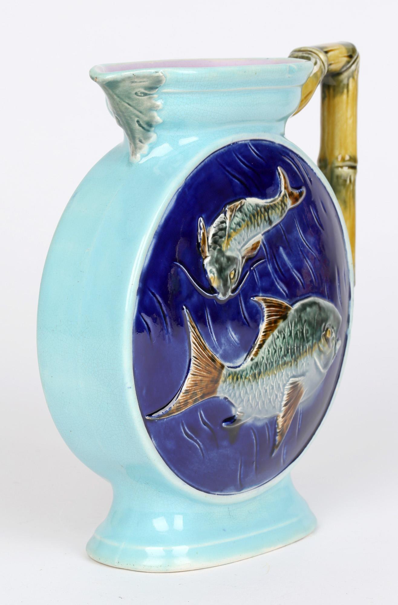 Pottery majolica glazed handled jug or rounded moon shape decorated in relief with two swimming fish by Joseph Holdcroft and with date marks for 1877. The jug is hand painted in tones of green, brown, blue and yellow with pink glazes to the inner