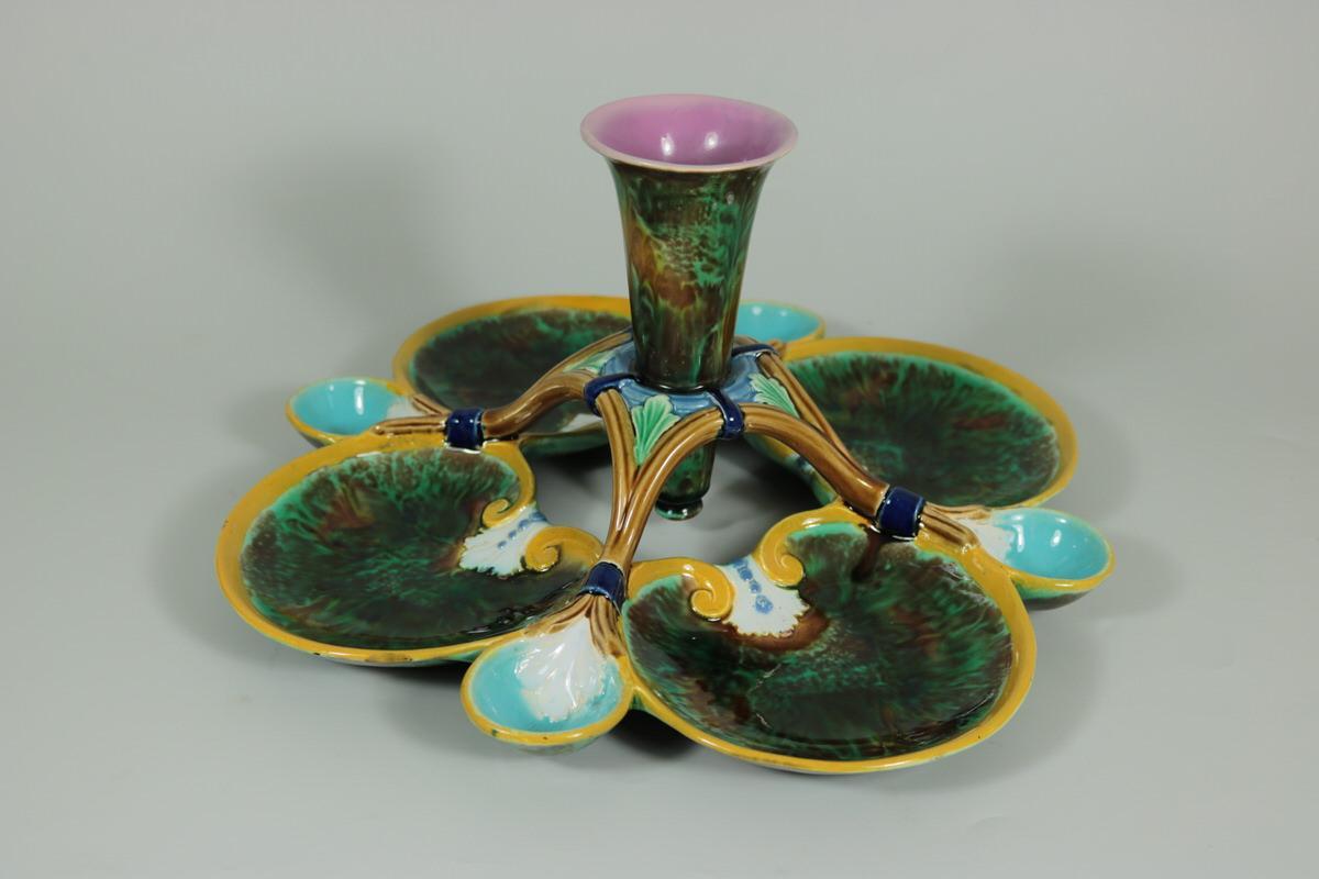 Holdcroft Majolica serving dish which features a central 'vase' receptacle, surrounded by four shell shaped dishes and four smaller spoon-shaped dishes. Coloration: Green, turquoise, yellow, are predominant.