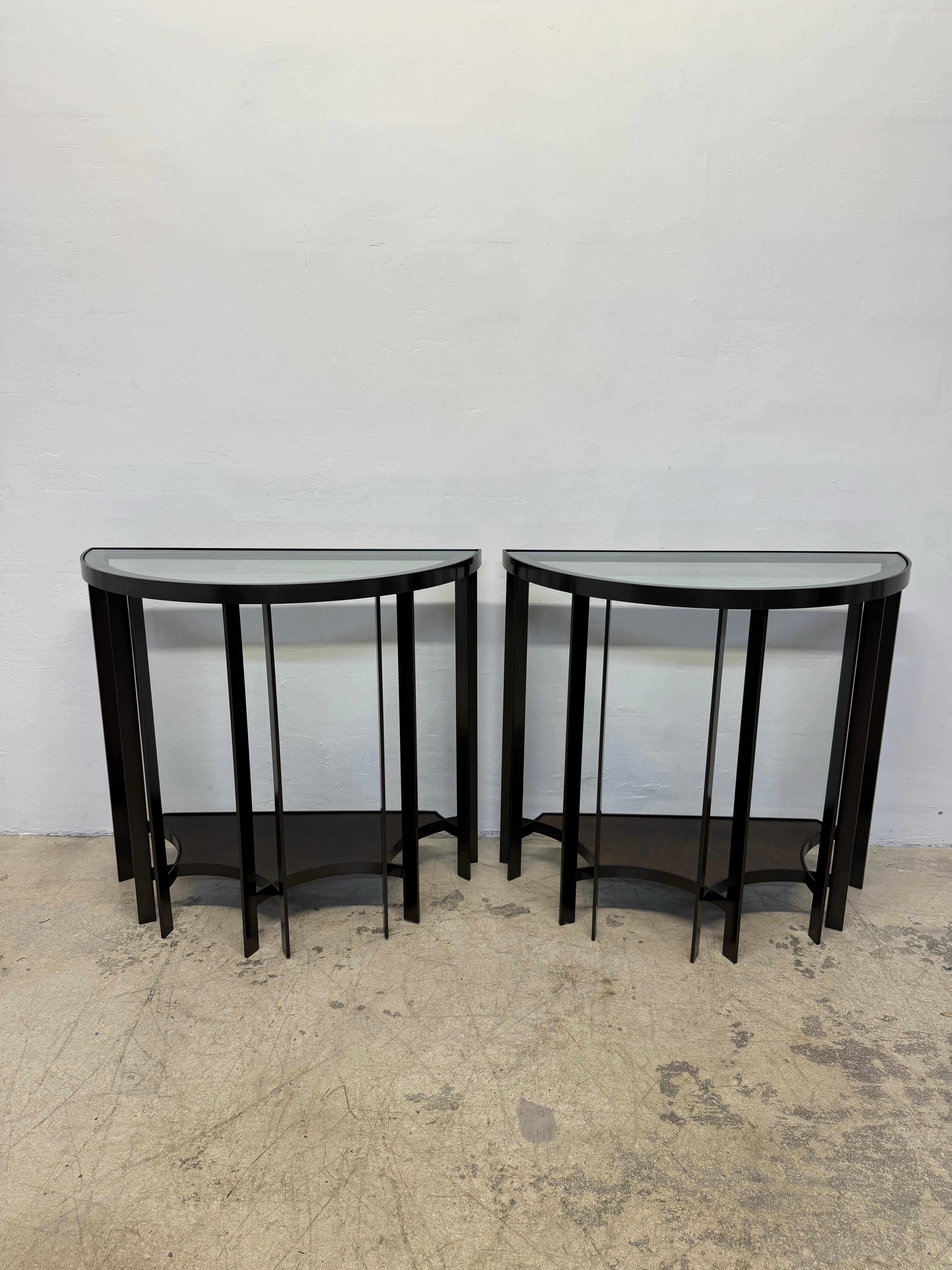 Pair of solid bronze base Demilune console tables designed by Joe Jeup for the Legacy Collection by Donghia. The hand rubbed dark finish bronze frame holds a top glass shelf as well as a wood lower shelf. Maintains original seal with signature of