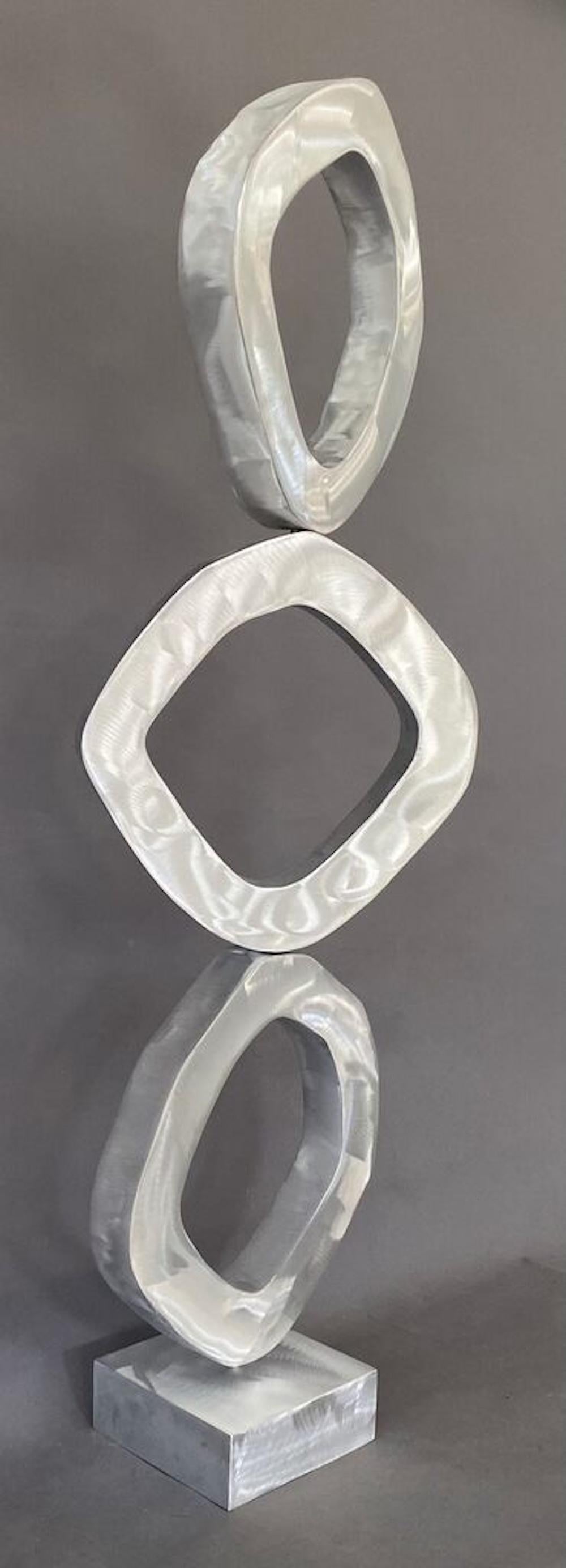 Trinidad 2025
Edición 2/10
Aluminio cepillado, con revestimiento transparente, cada pieza gira 360 grados, la escultura consta de 4 partes de base y 3 círculos irregulares cada uno sobre un pasador.
 Joseph Meerbott lleva más de 30 años construyendo