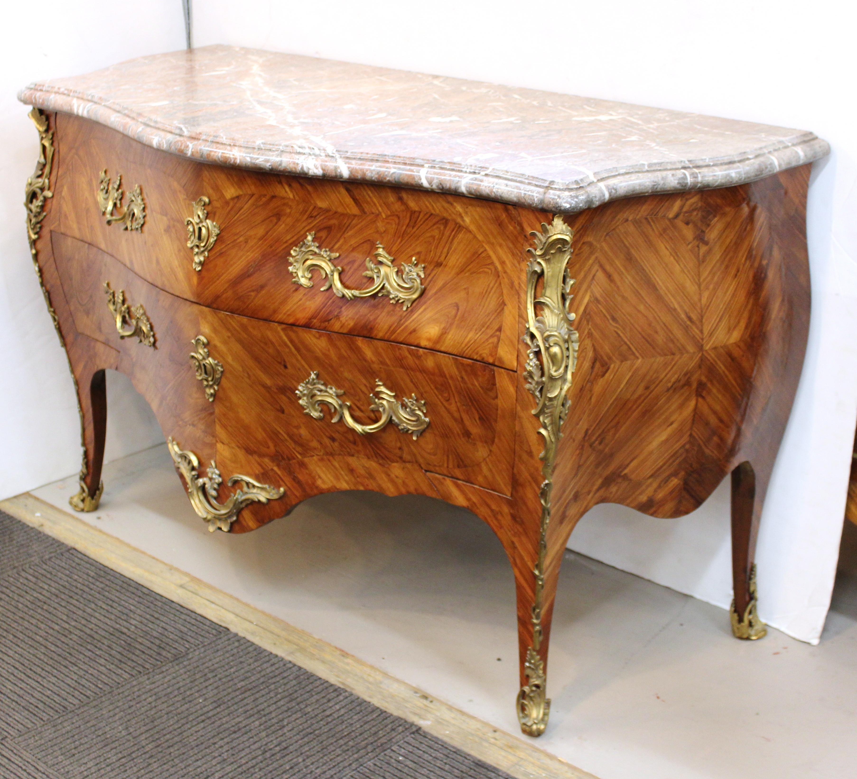 A French Louis XV period Kingwood veneer commode with ornate ormolu detailing, stamped with the obliterated signature of Joseph Schmitz and the mark of the Jurande.
The commode has a bombe contour and veneered in reverse-grained wood. Two drawers
