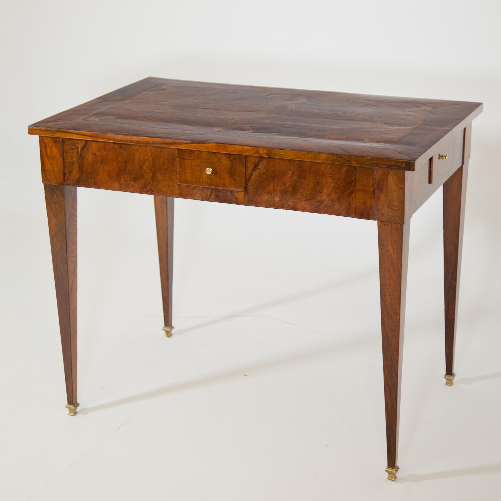Square table standing on tall tapered legs with bronze sabots and drawers on each side. The table top is veneered with strapwork and small ornaments in the corners and framed with a fillet ribbon. Walnut veneered.