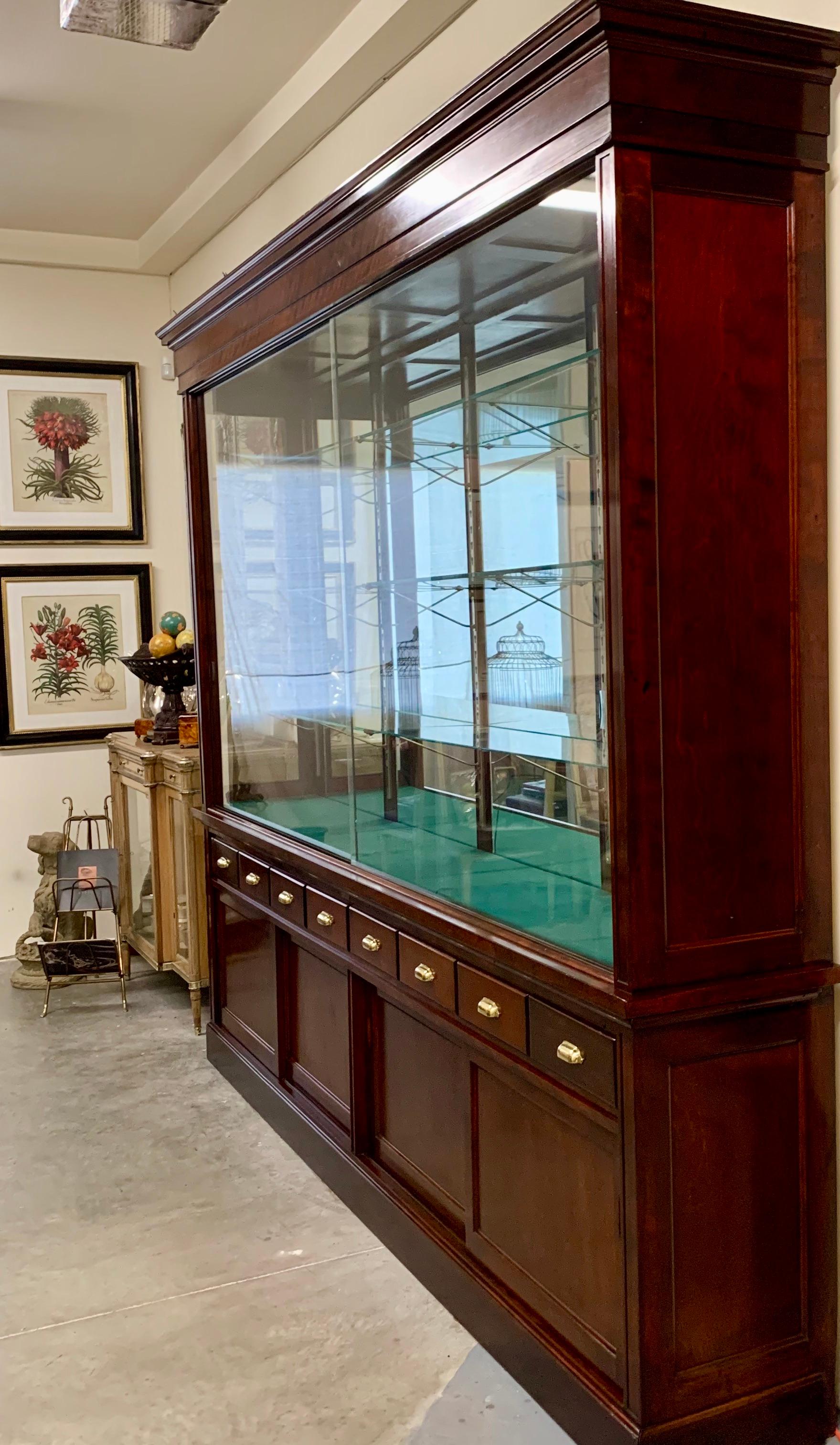 Large mahogany display cabinet made by the Joslin Showcase Company of Boston, Massachusetts. The company was founded in 1893. The cabinet is made it two pieces. The upper part has three glass shelves plus the bottom wooden shelf. The base has six