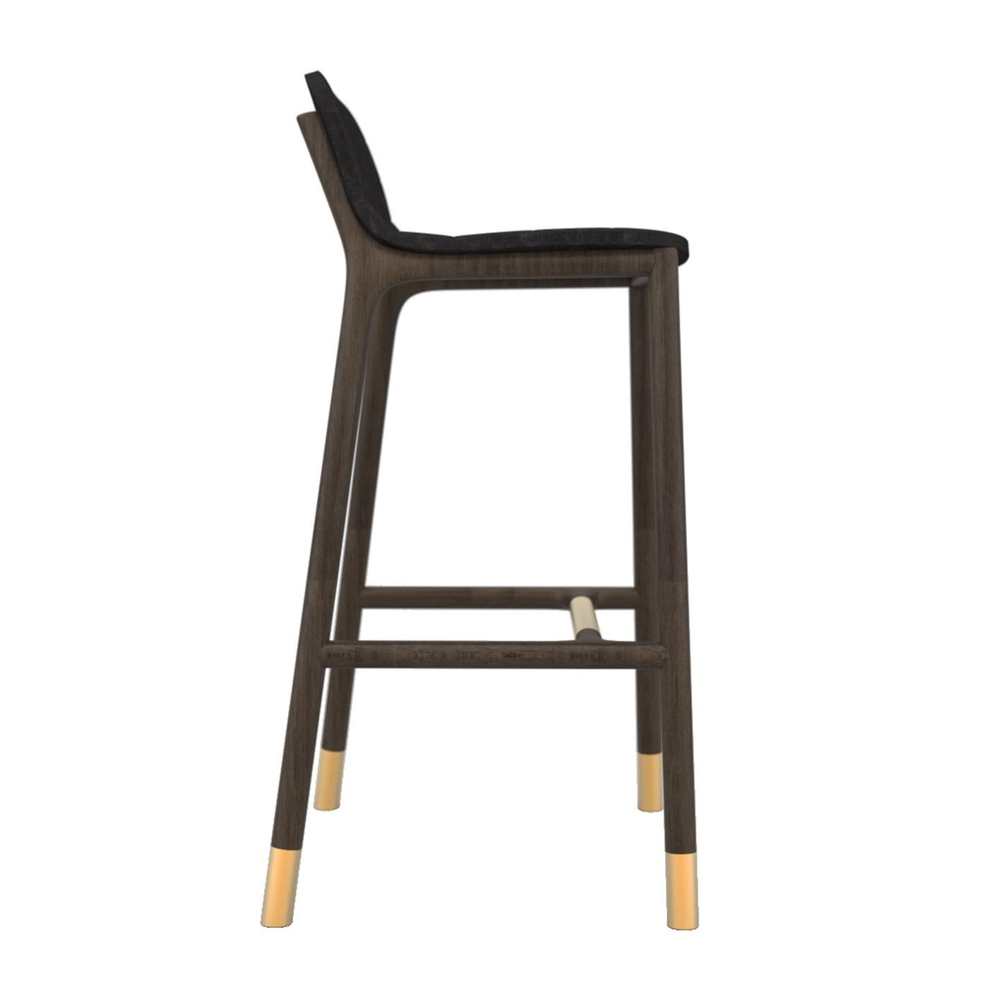 Exuding timeless elegance, this ash bar stool is distinguished by a linear, black-finished silhouette. The rounded seat is padded to provide great comfort, while luminous brass details add a precious accent to the footrest and slender legs. This