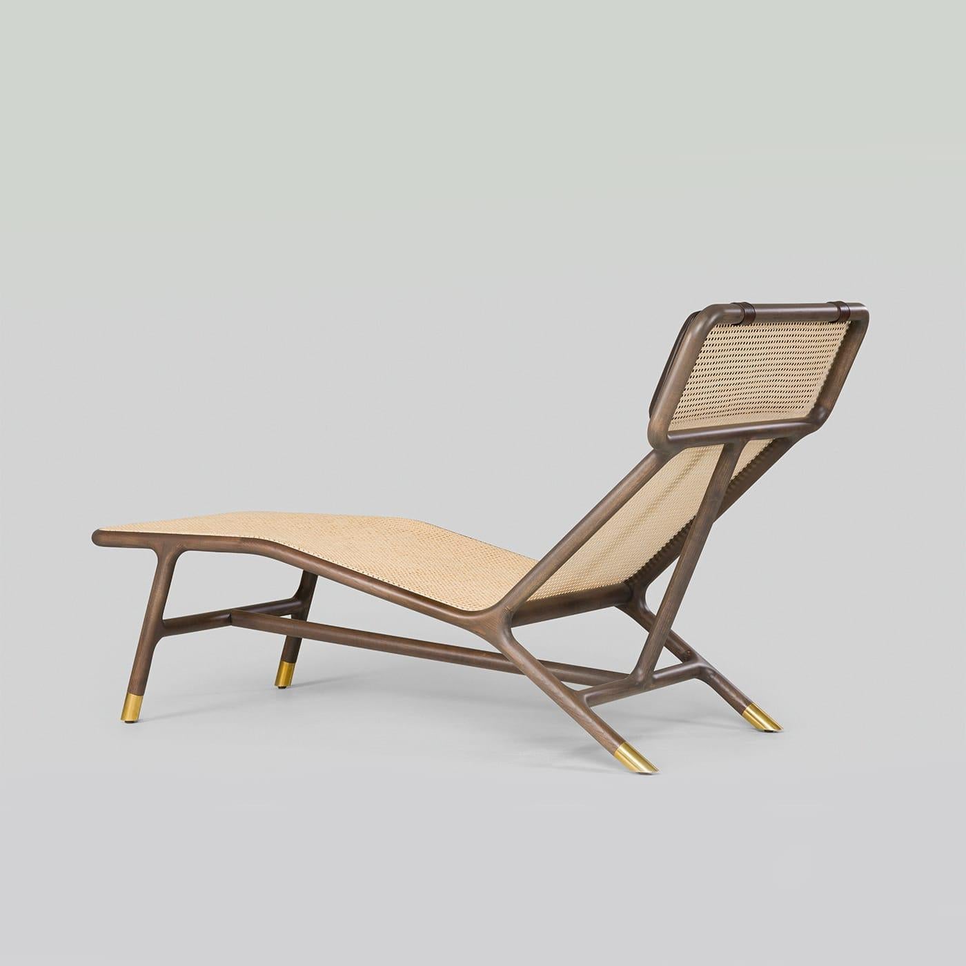 Une version moderne d'un classique intemporel, cette chaise longue raffinée présente une structure élégante en frêne marron avec des pieds détaillés en laiton et une assise emblématique en paille de Vienne. L'appui-tête est rehaussé par un coussin