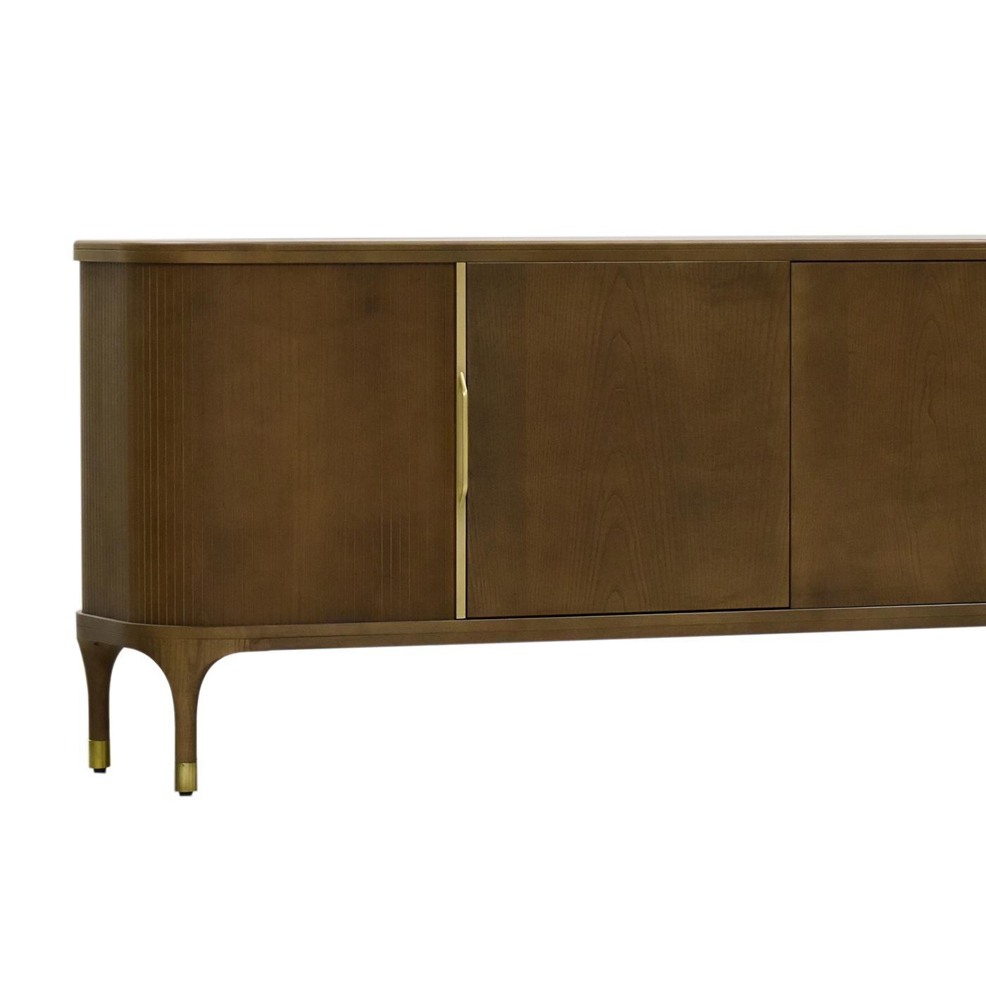 With its versatile design, crafted of walnut-finished ash, this sideboard will make a statement in both classic and mid-century decors. Its structure comprises four doors, the two in the corners sliding and with grooved texture, while the central