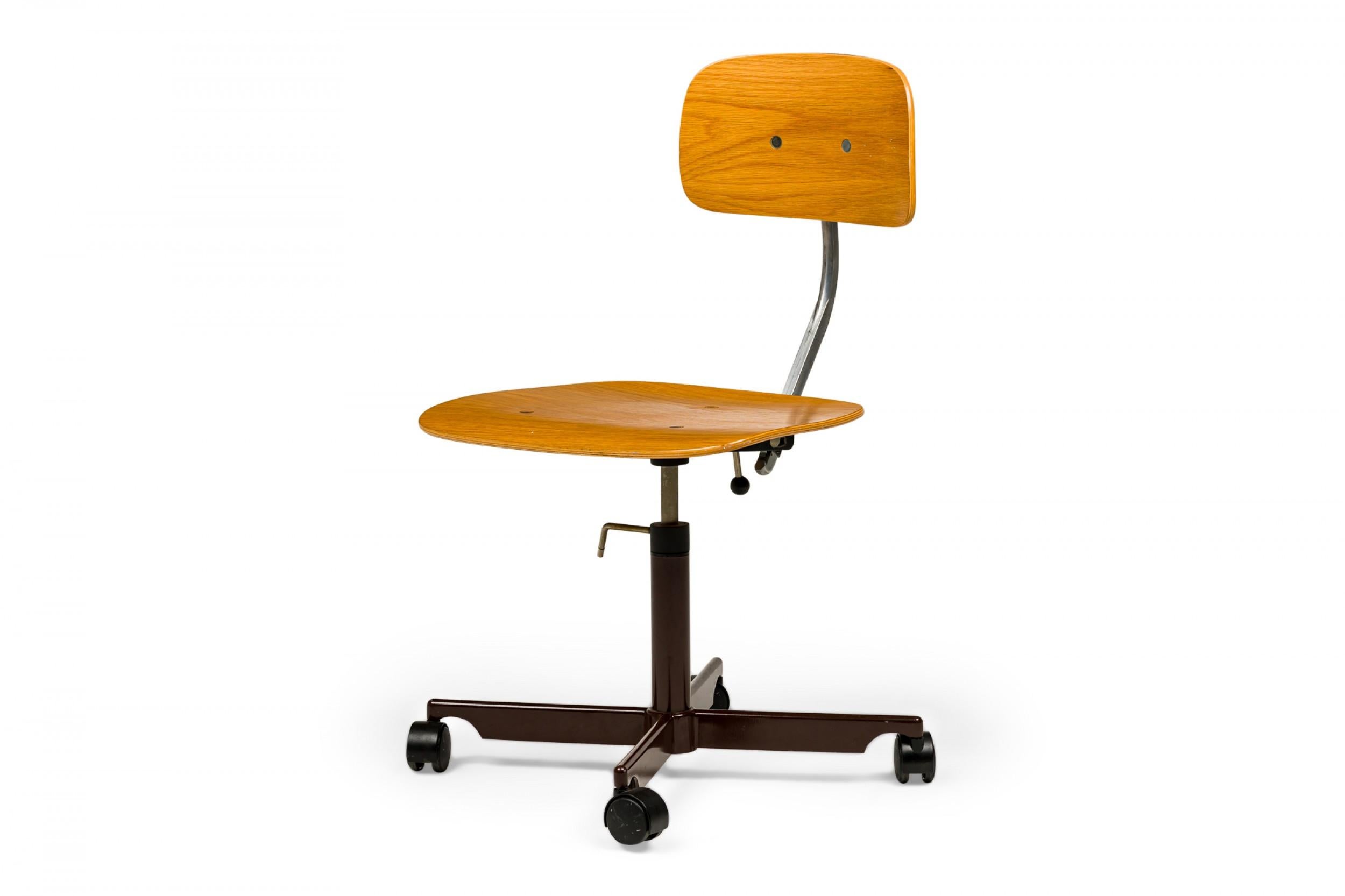 Chaise de travail danoise du milieu du siècle dernier avec assise et dossier en bois courbé de teck clair avec support de dossier réglable pivotant, reposant sur une base en métal revêtu de poudre brune avec quatre roulettes en plastique noir.