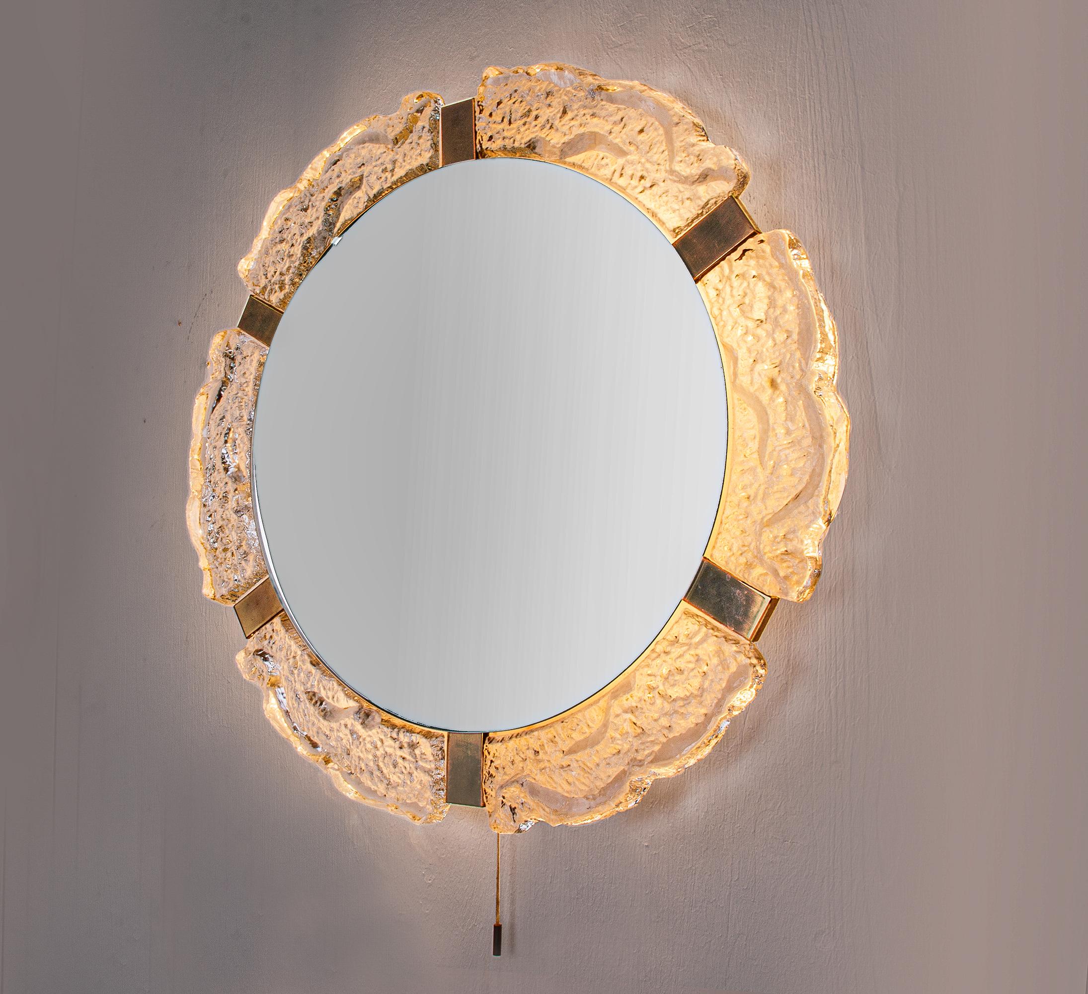 Elegante specchio da parete con sfondo illuminato. La cornice è realizzata in vetro di Murano color ghiaccio con ferramenta in ottone. Per uso intensivo. Prodotto da J.T. Kalmar, Austria, negli anni '60. 

Misure: diametro di 55 cm, profondità di 10