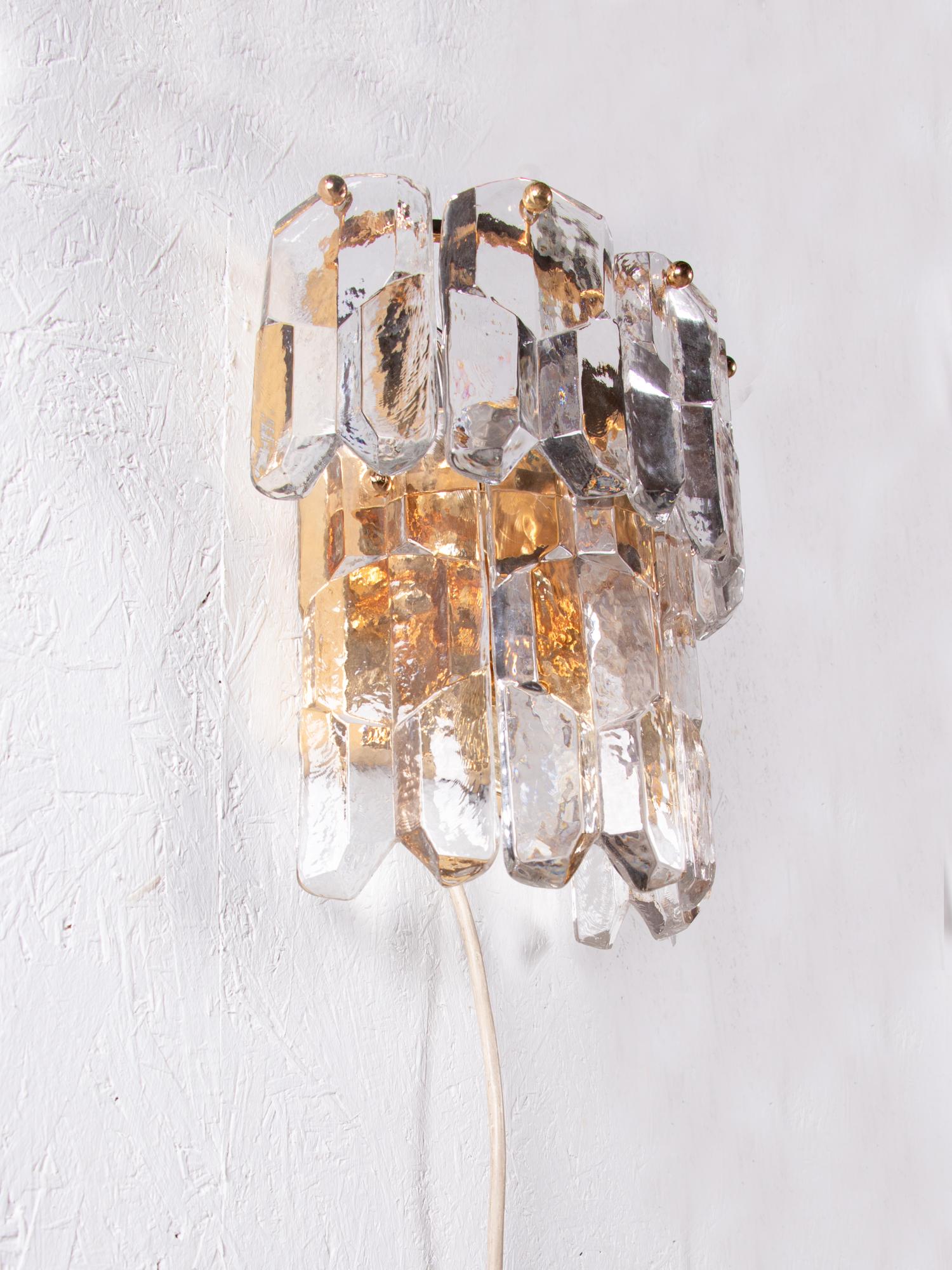 Elegant glass wall light designed by J.T. Kalmar made of ice glass elements suspended on a gold plated metal backplate. Beautiful play of light when lit. Gem from the time. With this light you make a clear statement in your interior design. A real