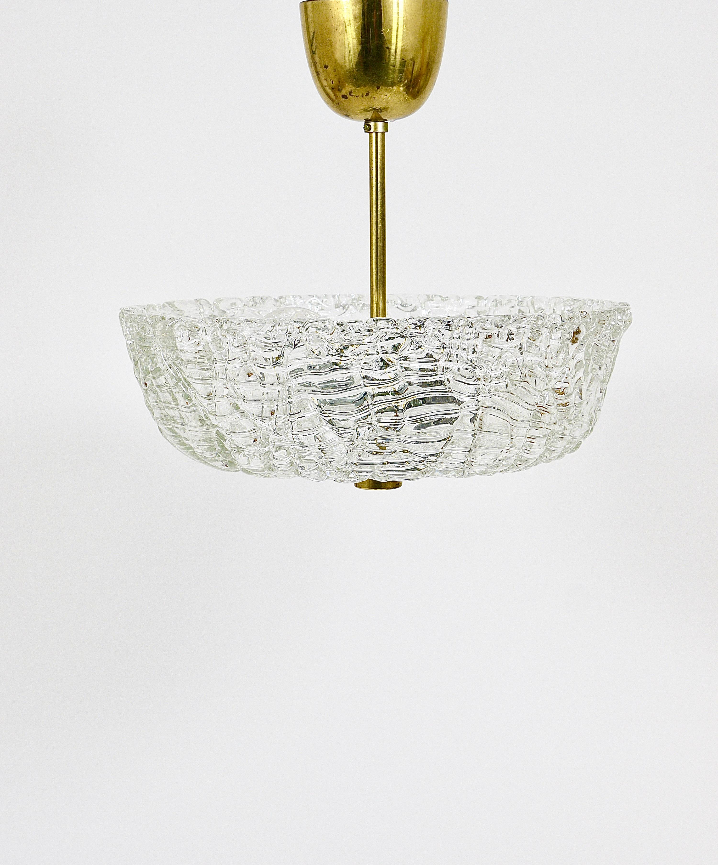 A beautiful petite round modernist brass and glass chandelier from the 1950s, manufactured by J.T. Kalmar in Vienna, Austria. This charming pendant light features a brass frame with a round lampshade made of clear, solid textured 