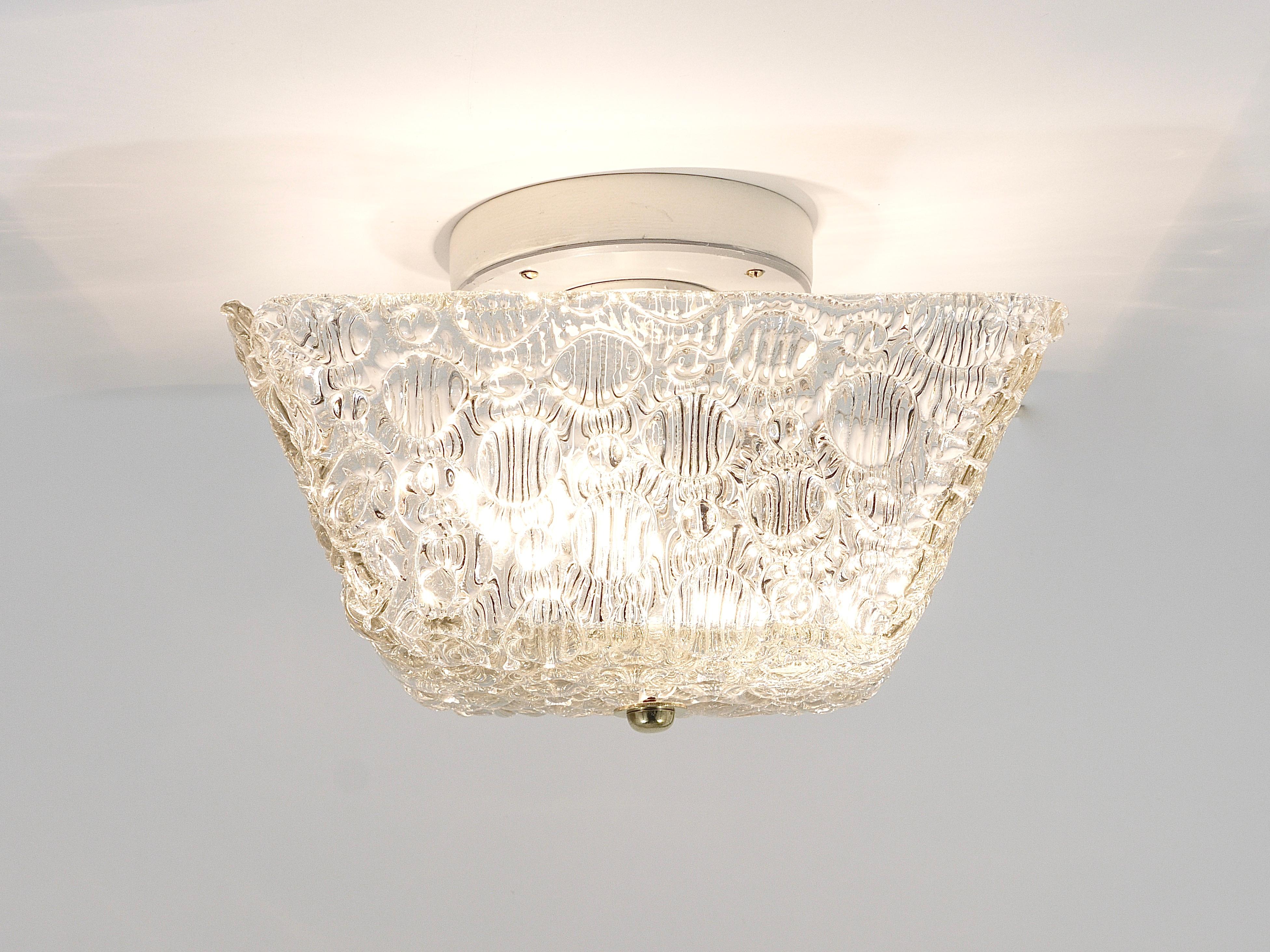 Introducing a charming Mid-Century flush mount or ceiling lamp. Crafted with a square lampshade from textured melting glass, reminiscent of ice, and adorned with a brass knob in the center. Manufactured by J.T. Kalmar Vienna / Austria in the 1950s,