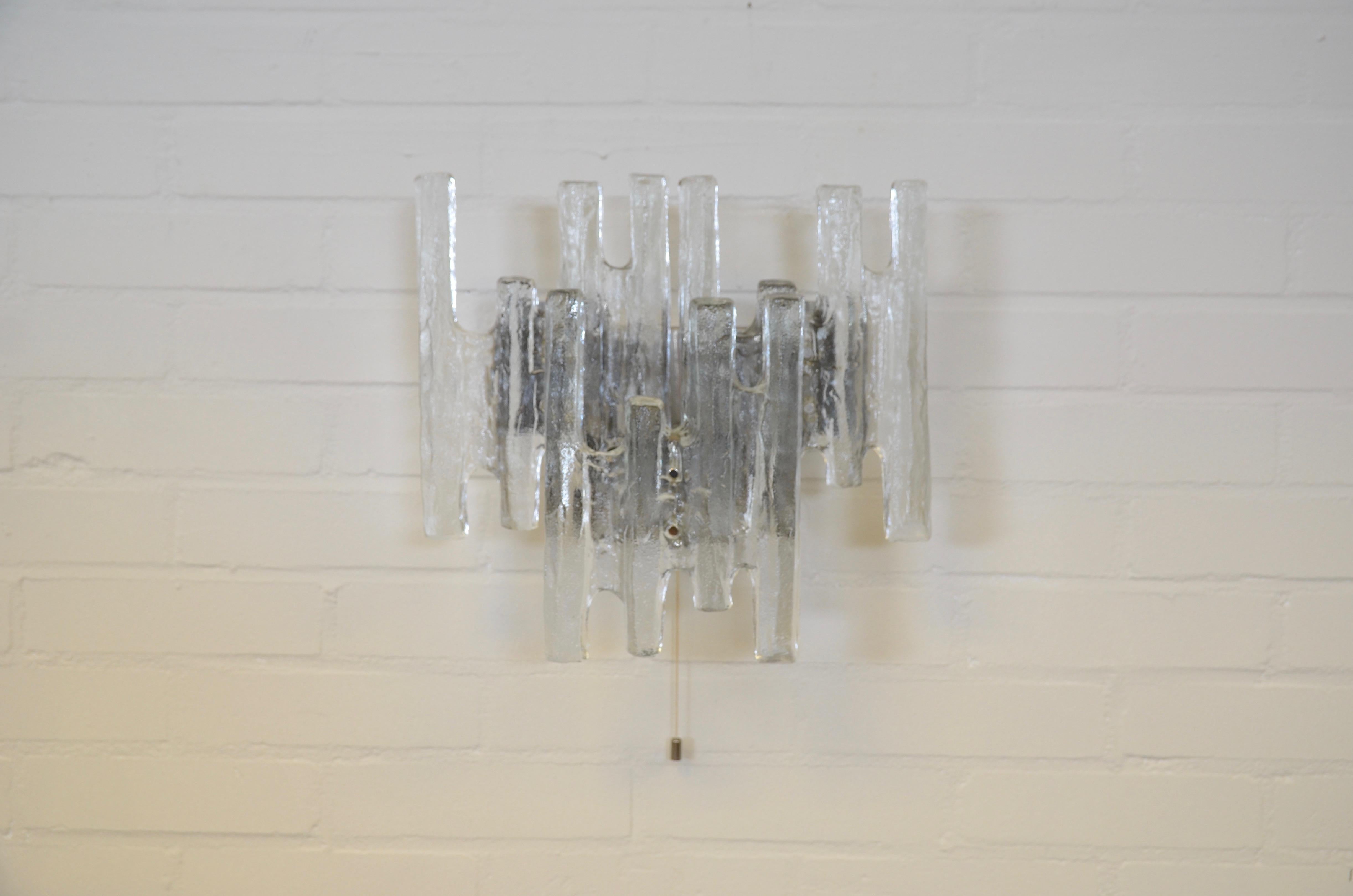 Heavy wall light in glass which looks like a piece of art. The lamp is named Pan, obviously referring to typical form a panflute. It spreads a wonderful light through the shape of the glass panel and the use of frosted glass. Three fixtures