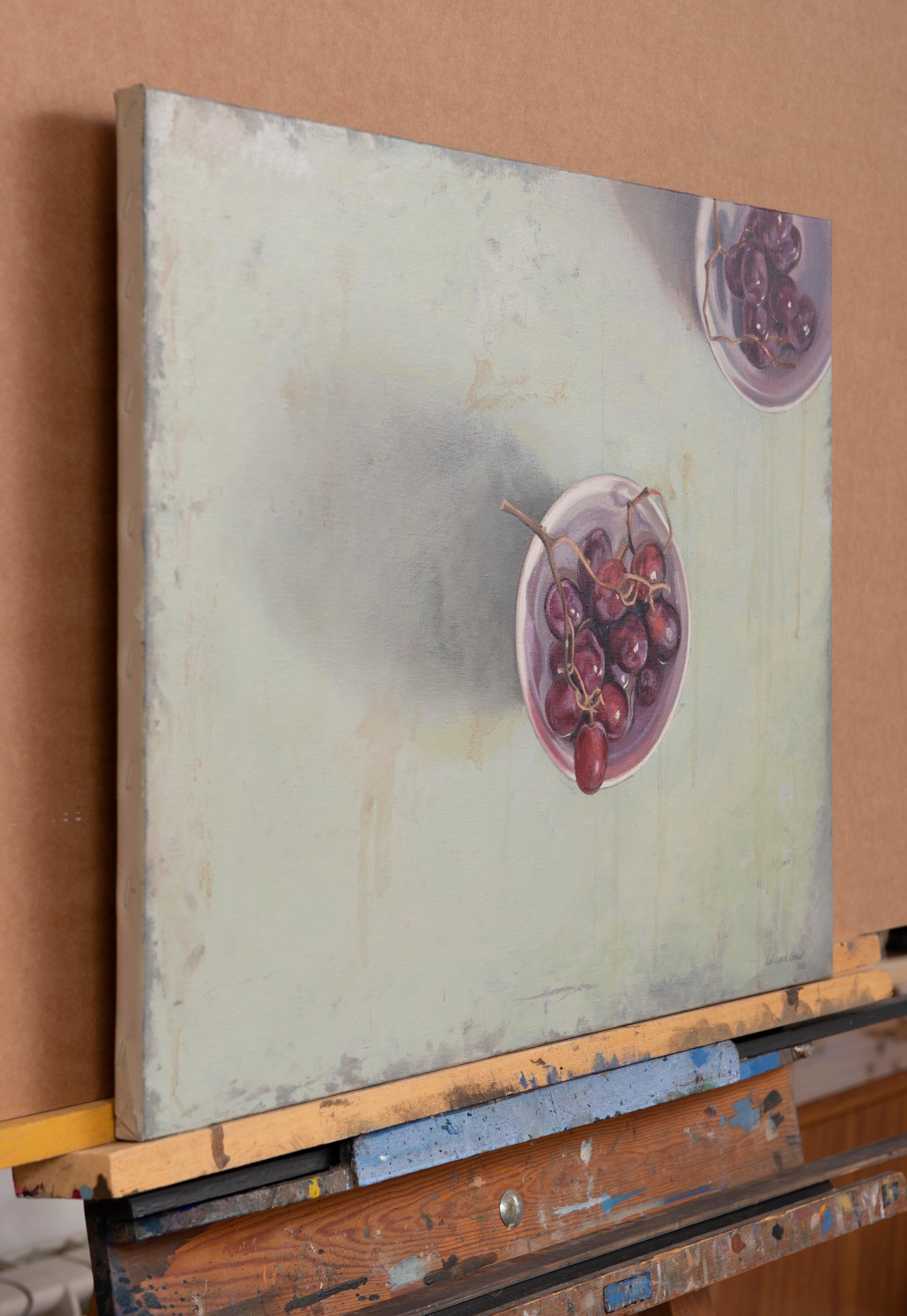 The artwork presents an intimate scene that invites a slow, thoughtful contemplation. Two bowls filled with water and red grapes are arranged in an unusual manner from a top-down view. One of them occupies the center of the composition, immediately