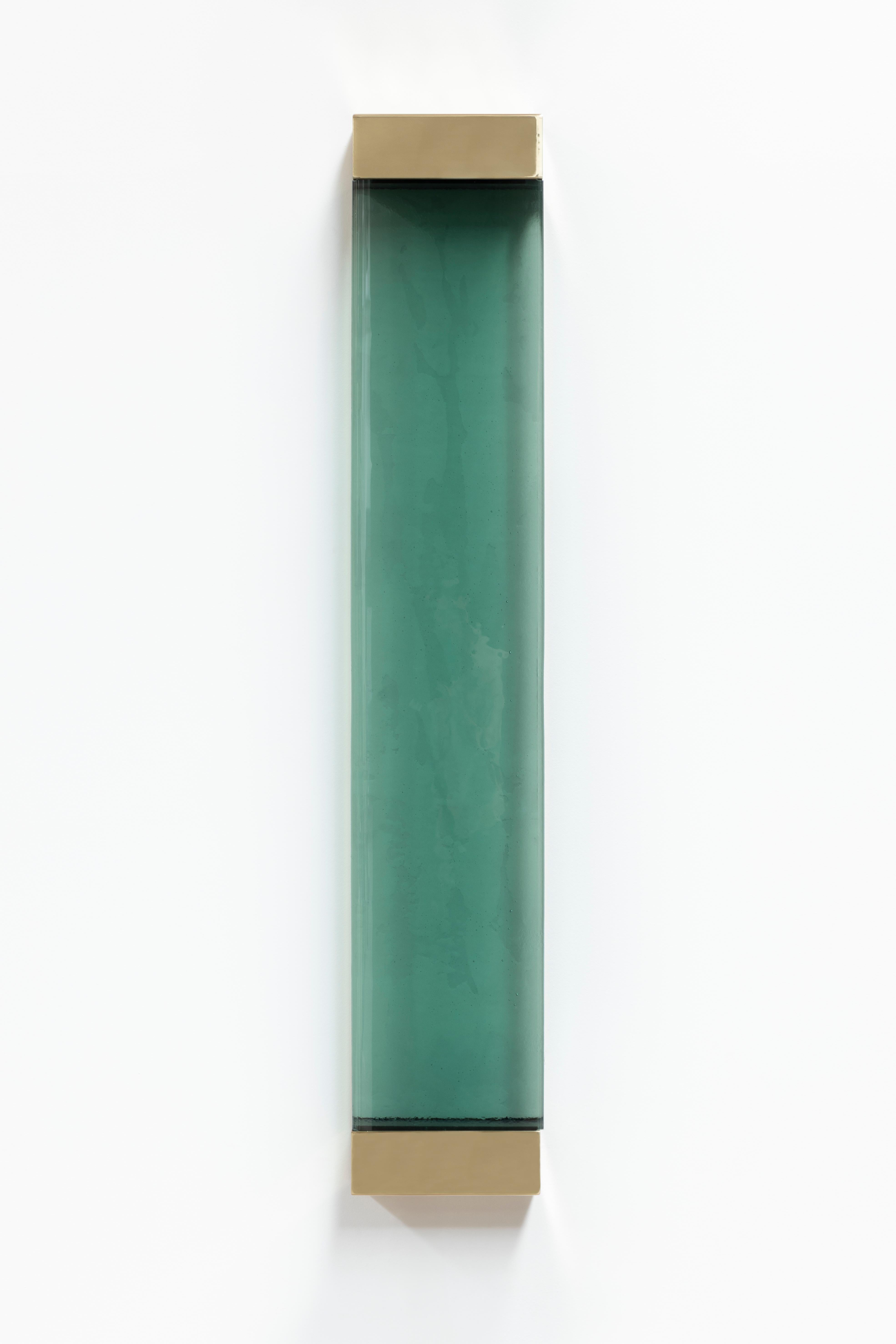 With its rigorous shapes and minimalistic contours, Jud wall lamp honors the aesthetic of Donald Judd. A geometric brass frame holds a translucent shaded glass pane concealing two colored resin filters, whose interaction with the strip LED generates