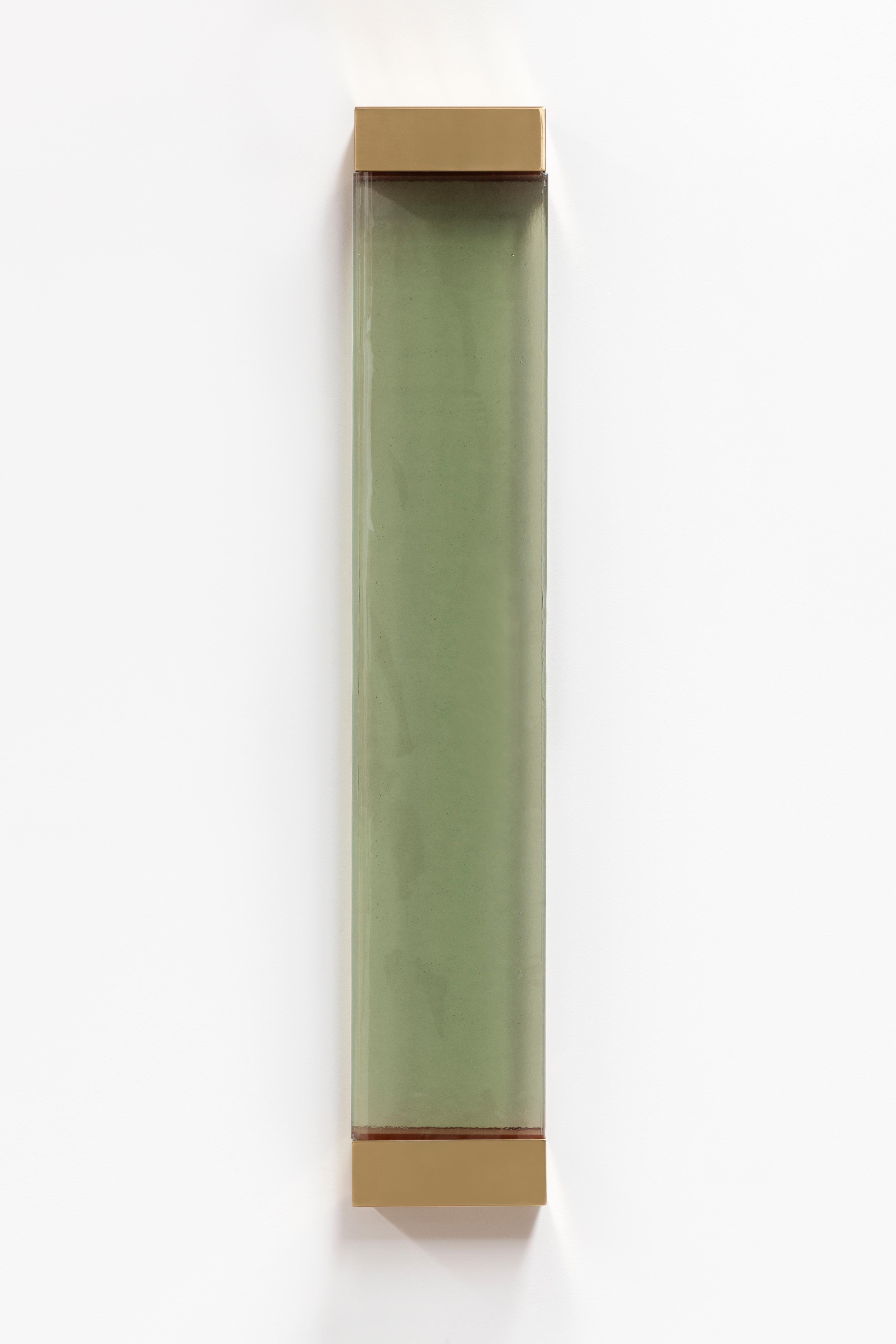 Avec ses formes rigoureuses et ses contours minimalistes, l'applique Jud rend hommage à l'esthétique de Donald Judd. Un cadre géométrique en laiton supporte une vitre translucide qui dissimule deux filtres en résine colorée, dont l'interaction avec