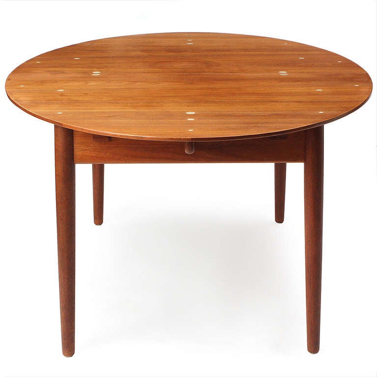 A rare and superb solid wood Judas dining table by Finn Juhl. Manufactured by Niels Vodder, the table features an expandable oval top (no leaves). Round silver inlays accents floating on a sculptural and architectural base with turned dowel legs.