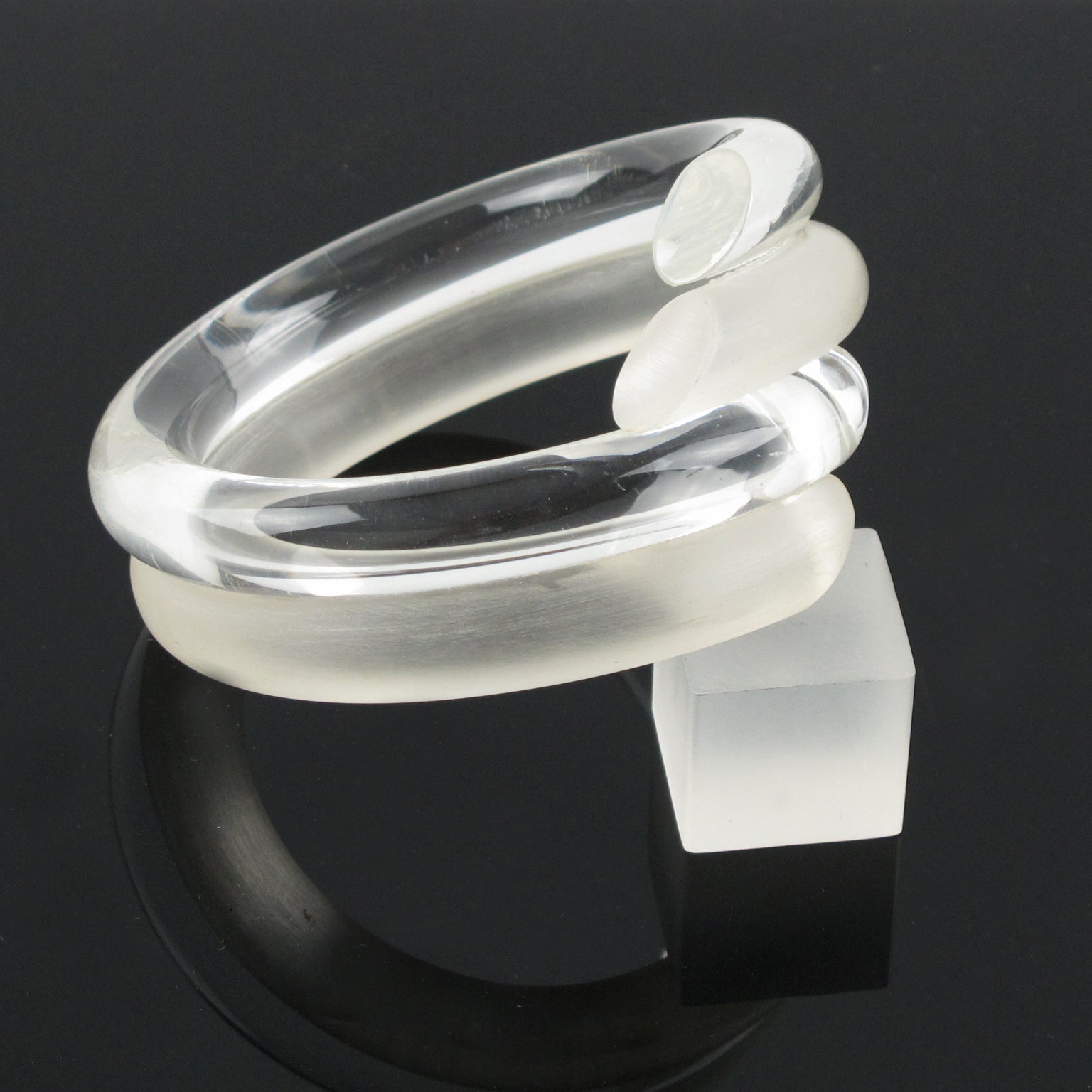 Judith Hendler designed this lovely Lucite or Acrylic bracelet bangle in the 1980s. This bracelet works on a contrast frosted and transparent color with a coiled-wrapped design. 
Judith Hendler is a famous Californian jewelry designer from the