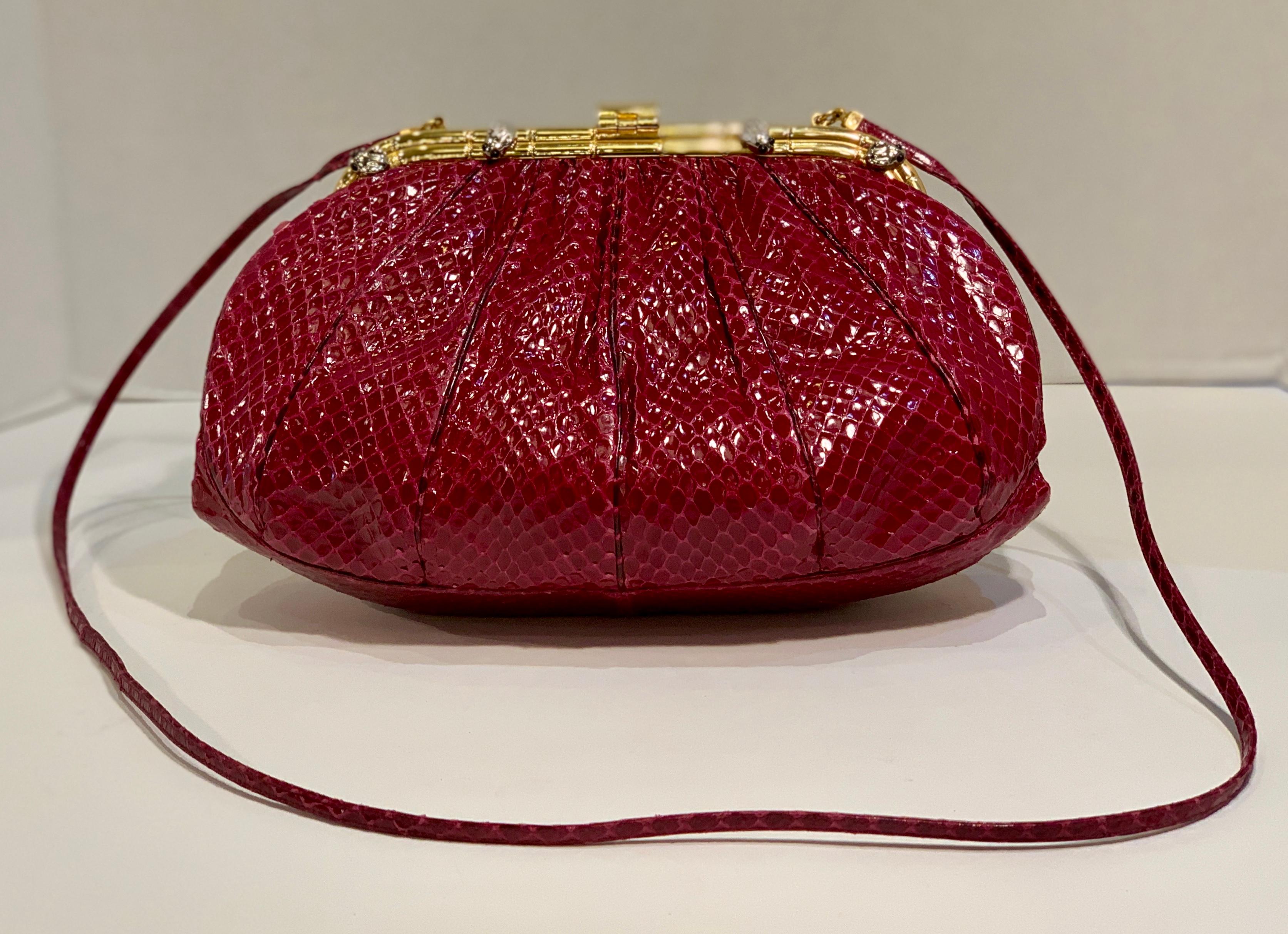 Collectible vintage Judith Leiber 1980's burgundy snakeskin leather evening bag, purse or clutch features a burgundy or wine-colored glossy snakeskin exterior gathered into a hinged gold metal frame at the top.  Frame with kiss top closure has a
