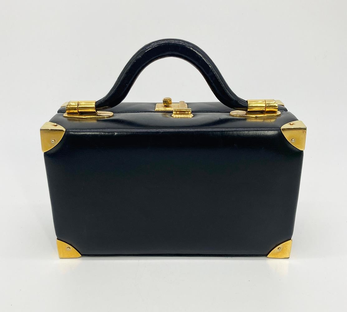 Judith Leiber Black Leather Box Handbag in good condition. black box calf leather trimmed with gold hardware. top slide latch closure opens to a black satin interior with 2 slit side pockets and a side strap to hold belongings. overall good