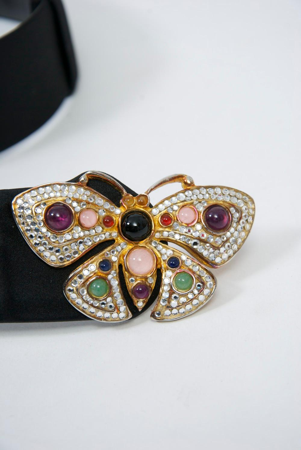 Elegant Judith Leiber black satin belt featuring a butterfly buckle composed of crystals punctuated by various colored cabochons. Belt is adjustable - one size fits all.