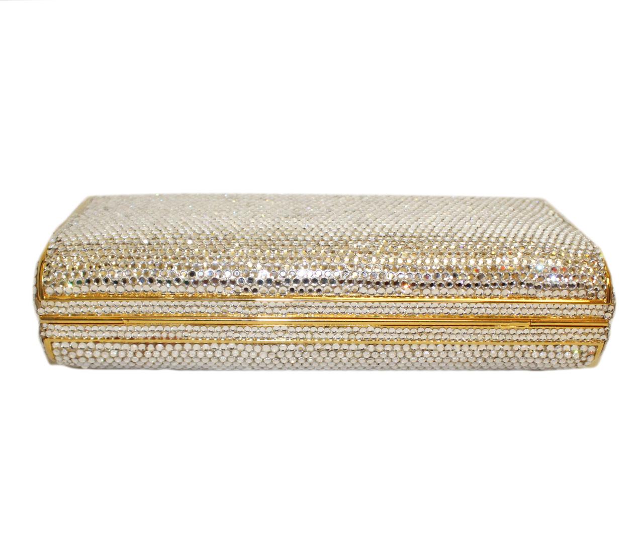 Judith Leiber clear crystal oblong clutch evening bag with gold tone frame includes a single snake shoulder chain.  The bag opens to a gold tone leather interior with a push lock closure at top decorated with a ruby color semi precious stone. Gold