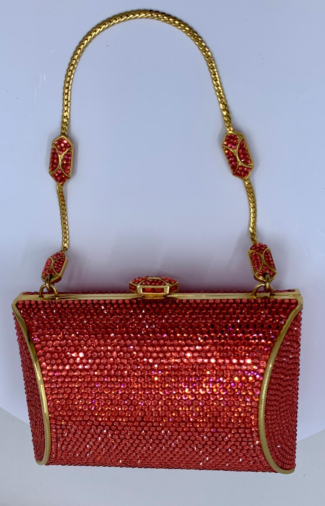 Exquisite handmade couture designer, Judith Leiber, crystal minaudiere evening bag or evening clutch is completely covered in coral colored crystals. Gold toned metal frame with metallic gold leather lined interior and a gold wrist chain is tucked