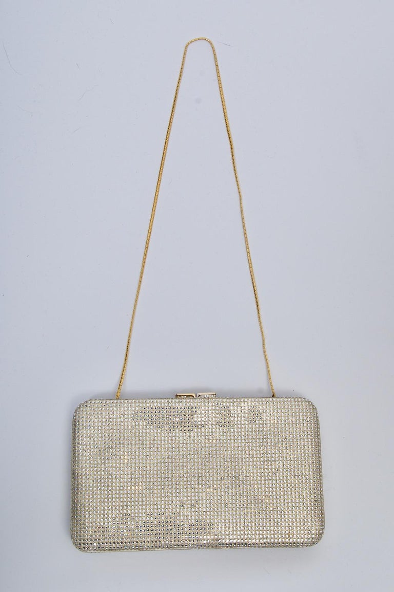 Judith Leiber essential evening clutch, the entire surface covered in clear crystals. Slightly rectangular in shape with rounded corners. Gold metal frame, crystal studded clasp, and gold chain that converts the clutch to a shoulder bag. Double
