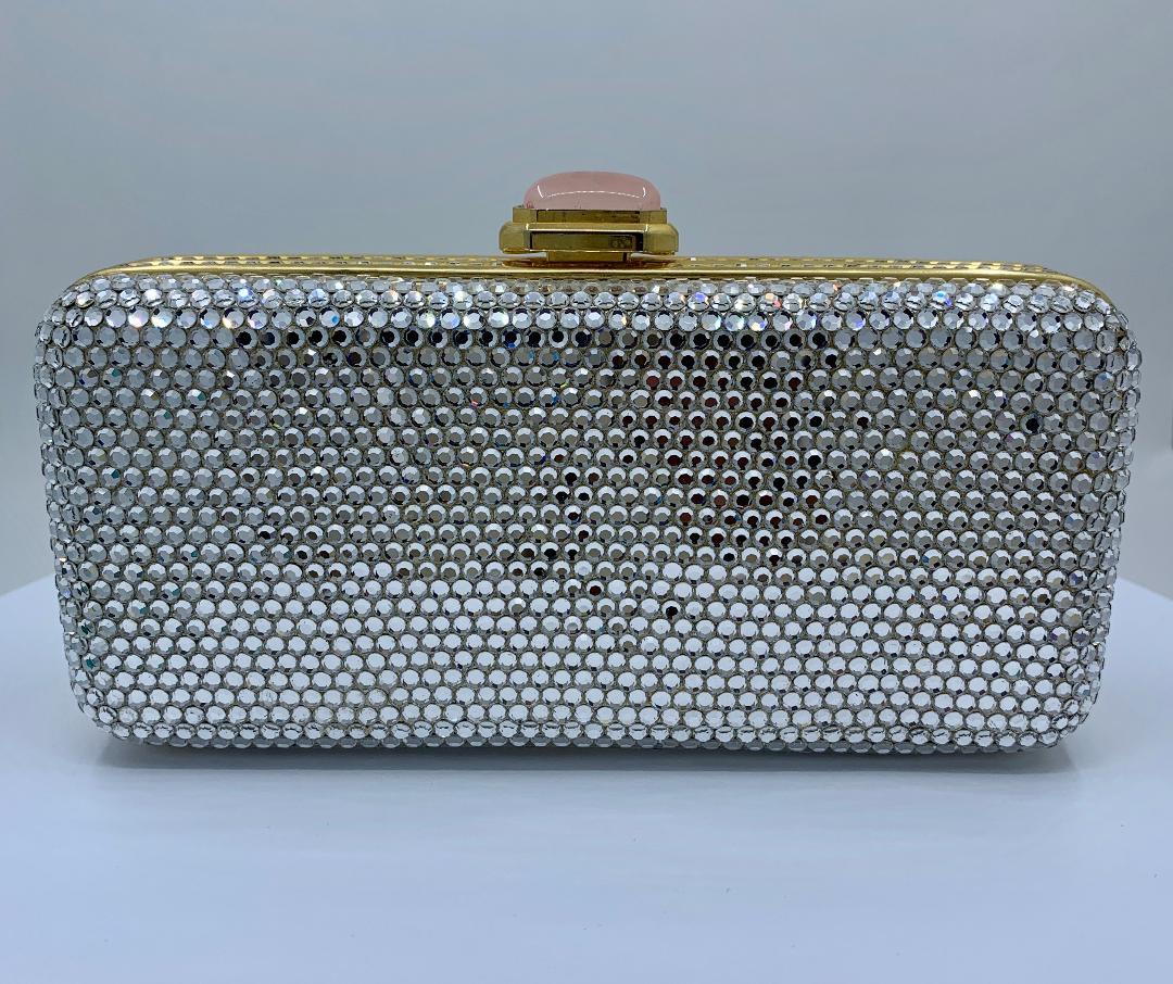 Timeless and elegant hand made couture designer Judith Leiber rectangular shaped minaudiere evening bag or clutch features a gold toned metal frame covered in dazzling silver crystals. Bag features a beautiful rose quartz cabochon push down closure