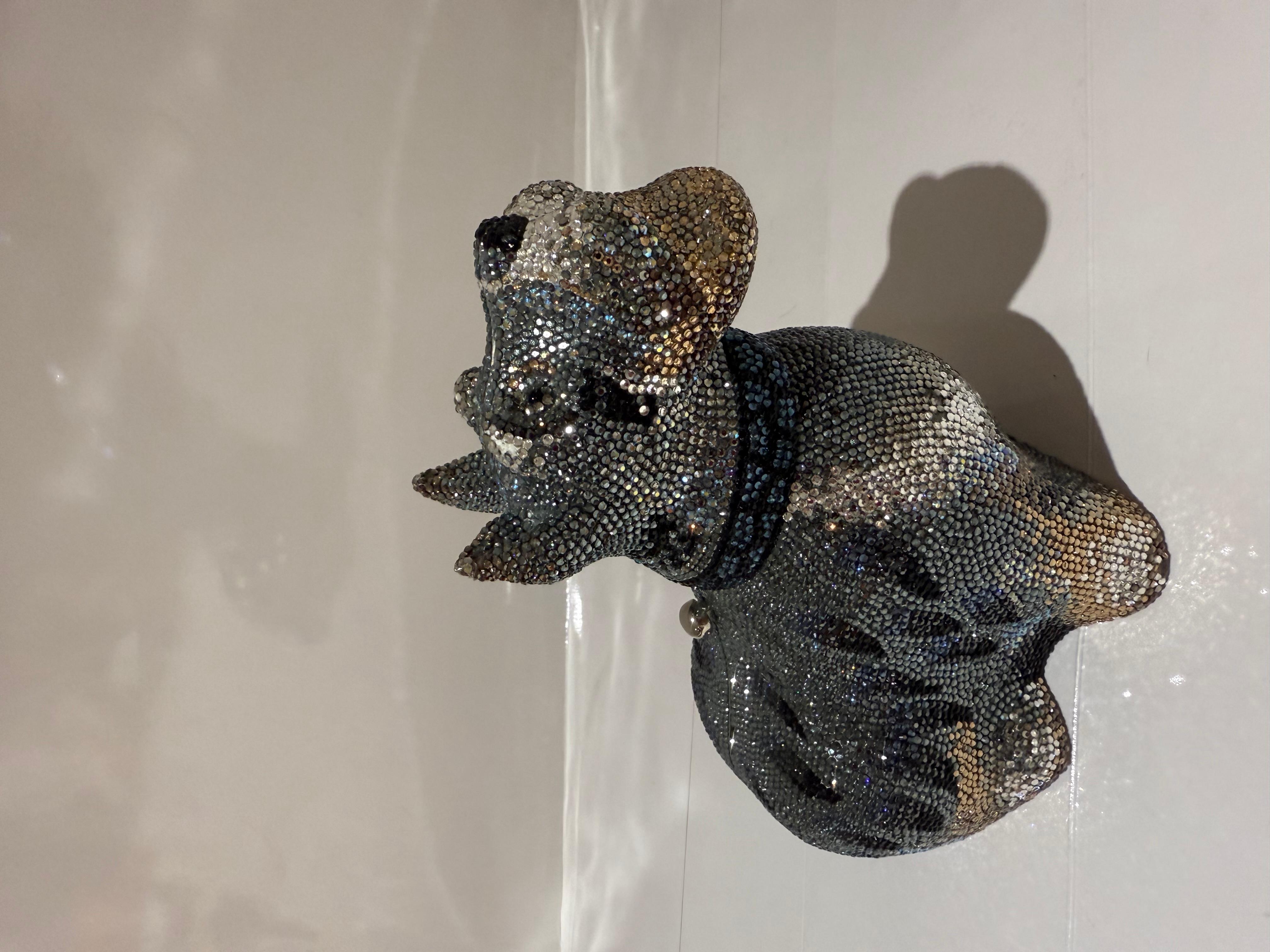 JUDITH LEIBER Crystal Terrier Minaudiere Clutch in  Multicolor. This petite clutch is entirely covered in crystals with a hard silver shell, in the shape of an adorable dog. This clutch opens to an interior of metallic silver leather with a thin