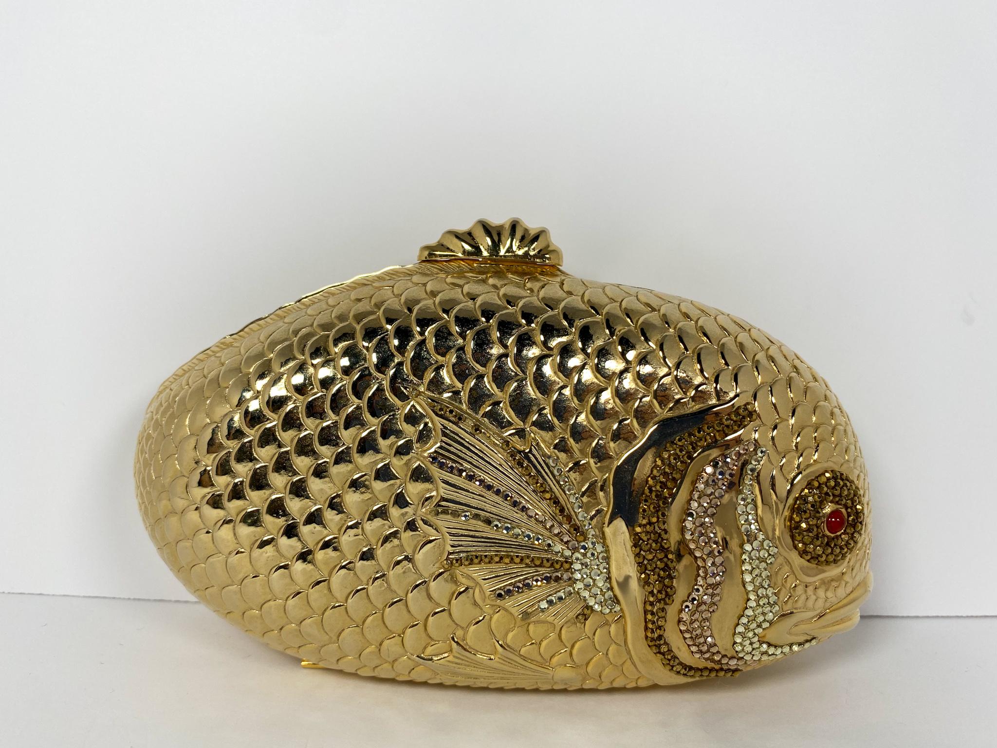 Gold-tone hardware in the shape of a fish with a push lock clasp, lightly covered in brown, gold, and silver toned Swarovski crystals.
		
Condition: Good used condition.
Exterior: Some loose and missing crystals.
Interior: Lined with leather, split