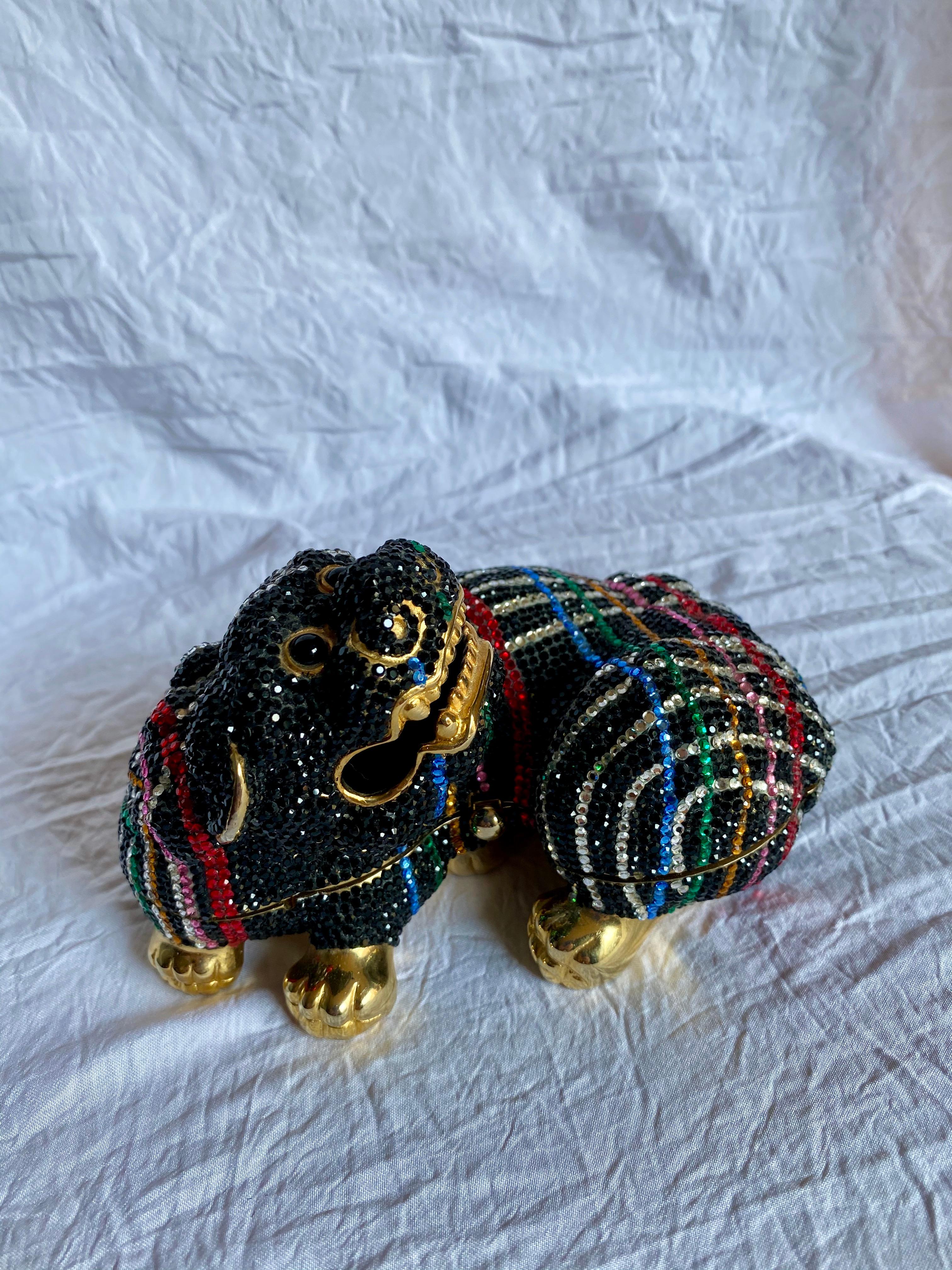 Leiber’s classic Foo Dog minaudiere made with gold-tone hardware covered in striking black swarovski crystals and silver, blue, green, yellow, pink and red crystals set in a crosshatched design. This bag features a push lock clasp that currently