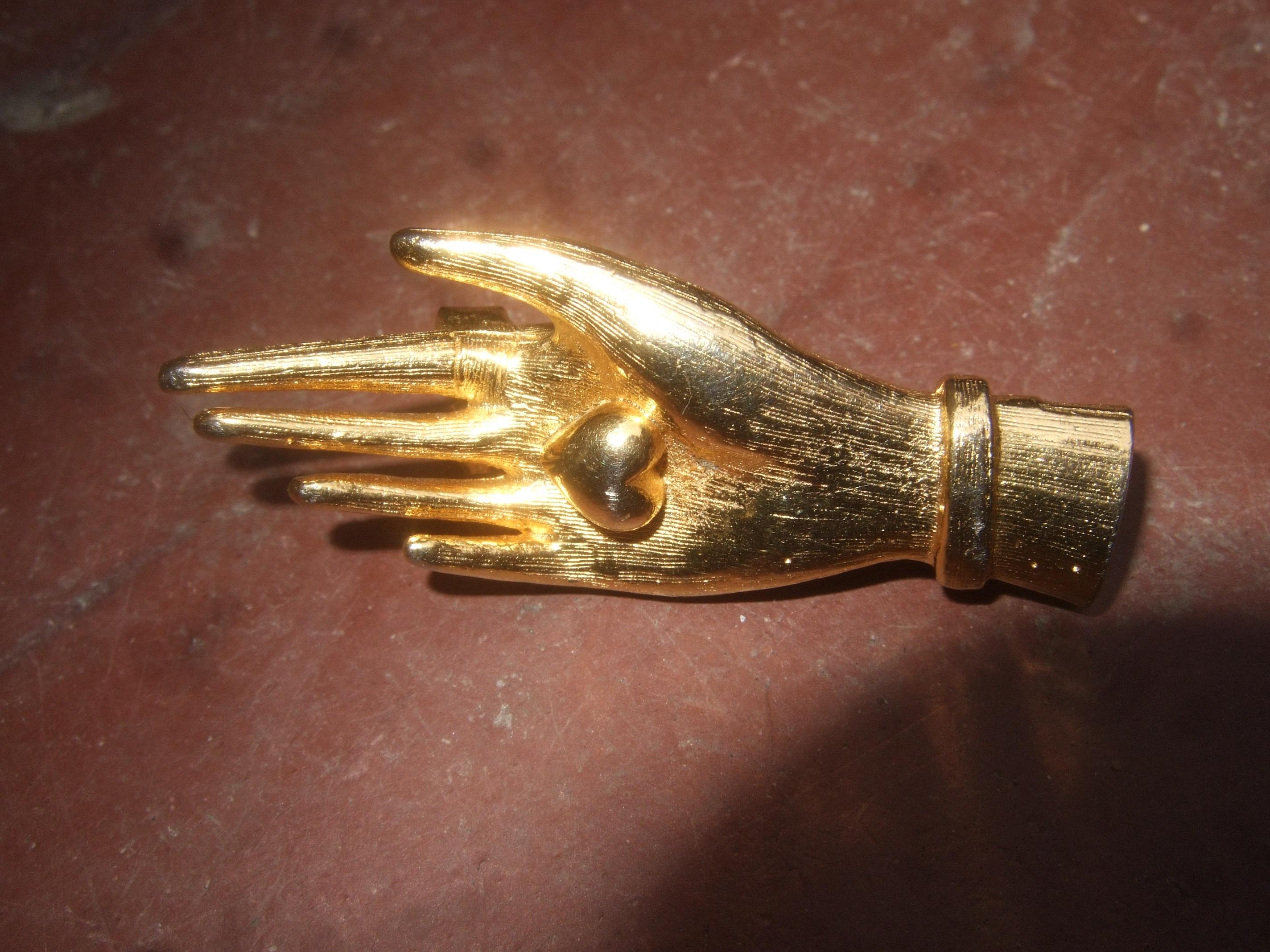 Judith Leiber Gilt metal diminutive size figural hand brooch c 1980s
The unique stylized hand brooch is sheathed with luminous gilt metal
The palm of the hand is holding a small size heart 

Makes a charming compact size accessory pinned on a lapel,