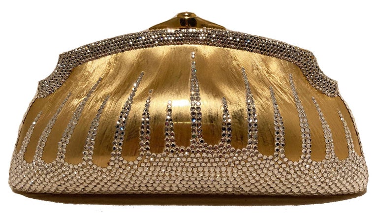 Judith Leiber Gold Clear Swarovski Crystal Minaudiere in excellent condition. Gold metal exterior trimmed with clear swarovski crystals. Top button closure opens to a gold leather interior with 2 separate compartments and an attached gold chain