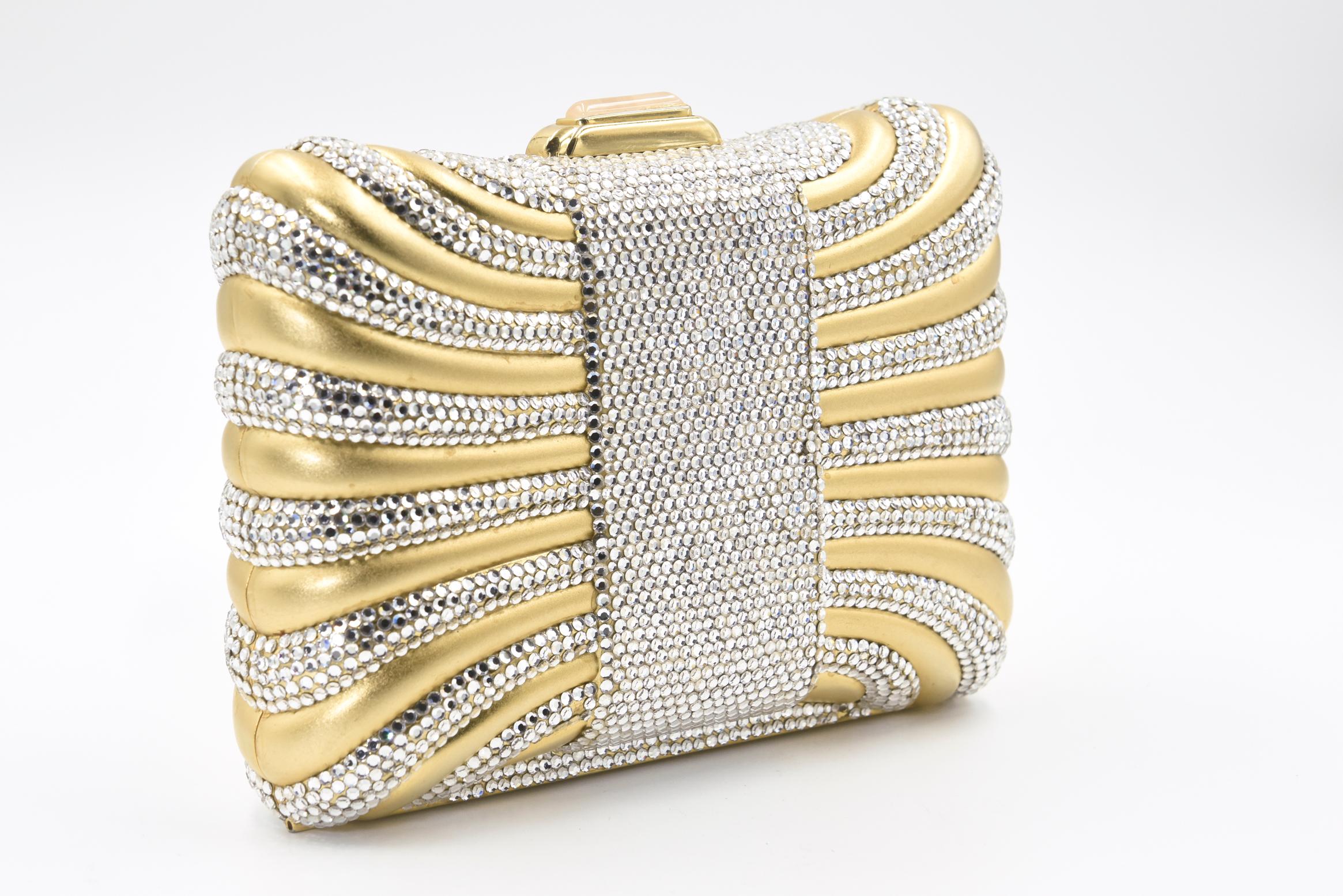 Die elegante Judith Leiber Minaudière sieht aus wie eine Geschenkbox oder ein Kissen mit einem Swarovski-Kristallband.  Die Tasche verfügt über einen Kristalldruckverschluss mit  goldene Beschläge, der Schulterriemen, der in das Innere der Tasche