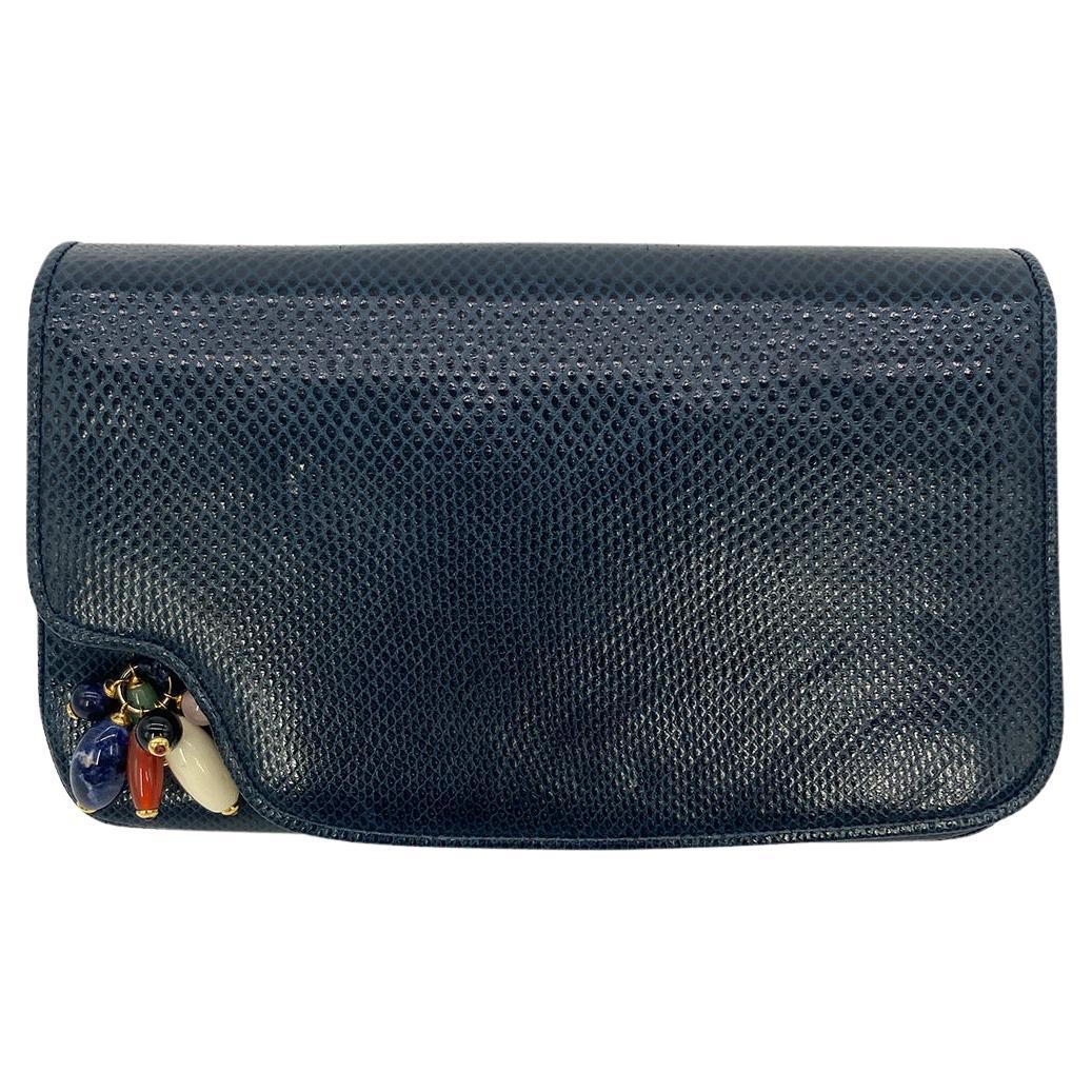 Judith Leiber Navy Lizard Gemstone Beaded Clutch in good condition. Navy lizard leather trimmed with gold hardware and multi color gemstone bead detail along front. Lift flap closure opens to a navy nylon interior with one slit and one zipped side