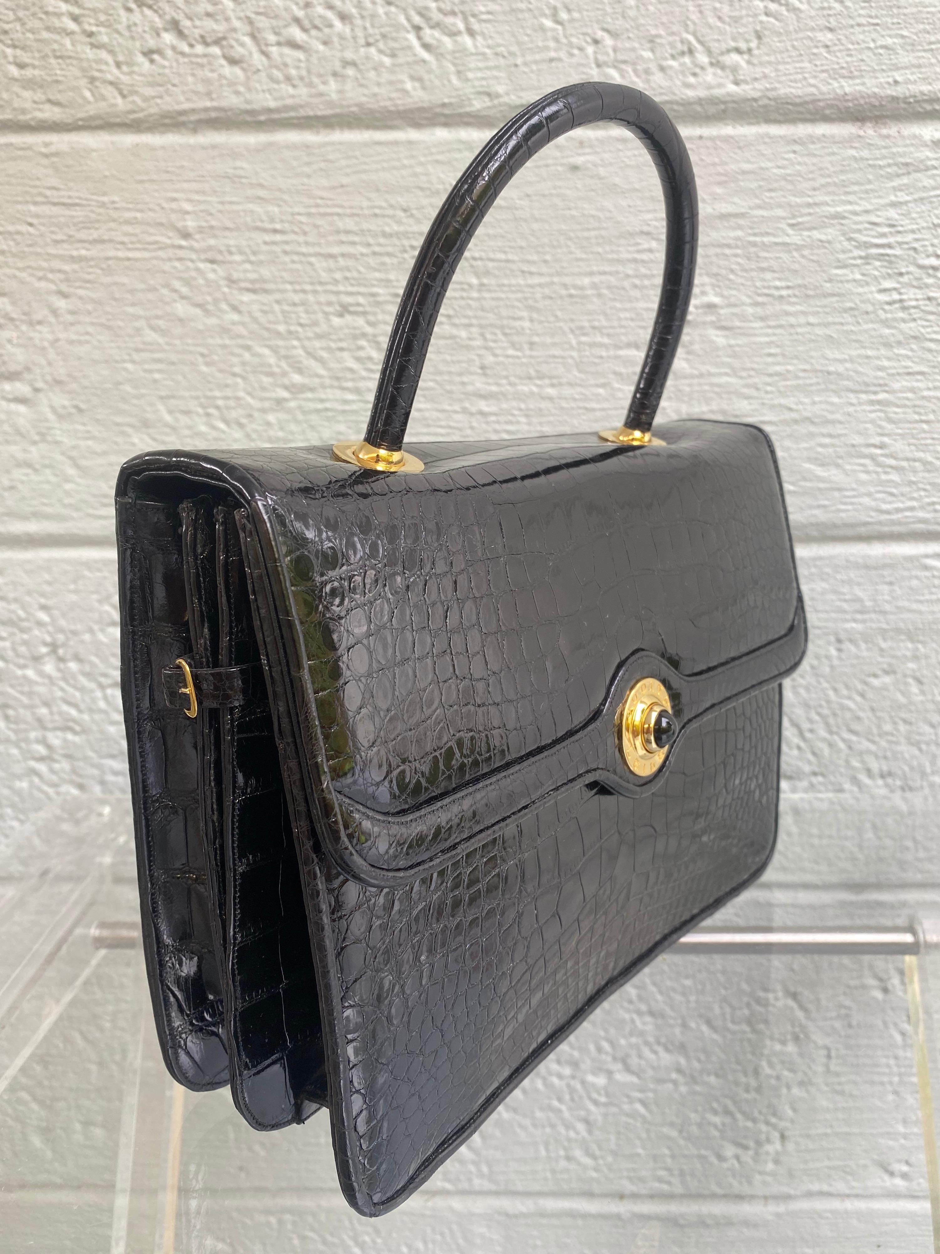 The Vintage Kelly Flap style Alligator bag from Judith Leiber is one of the famed luxury goods house's most coveted and exclusive items. This flap bag is bathed glazed black glossy alligator. Judith Leiber is engraved in gold. Goatskin black leather