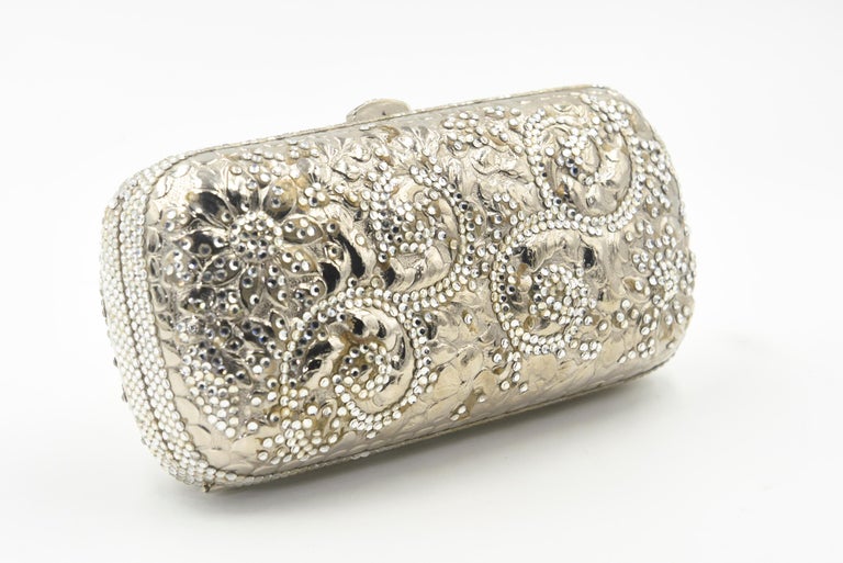 Elegant Judith Leiber silver metal and crystal oblong evening bag clutch featuring a scrolling foliage flower design on a silver - toned metal bag.  The hardware is silver.  It has a silver leather interior with a silver shoulder strap that can be