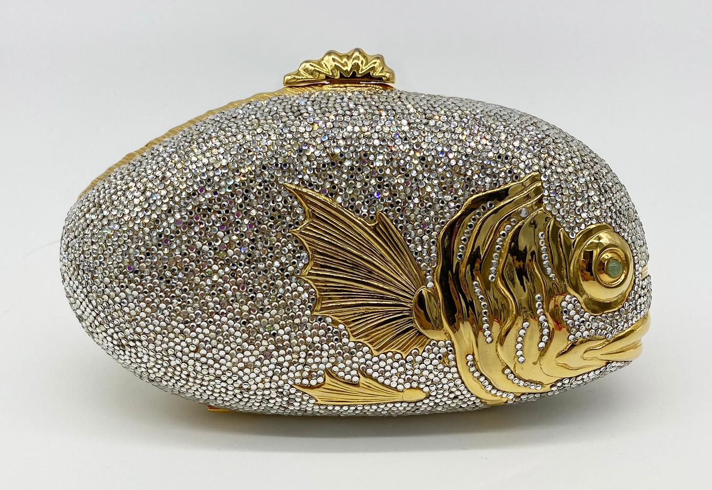 Judith Leiber Swarovski Crystal Fish Minaudiere in very good condition. Unique fish shape minaudiere covered in clear swarovski crystals with gold metal body. Jade green cabochon eyes. Top sliding latch closure opens to a gold leather interior with