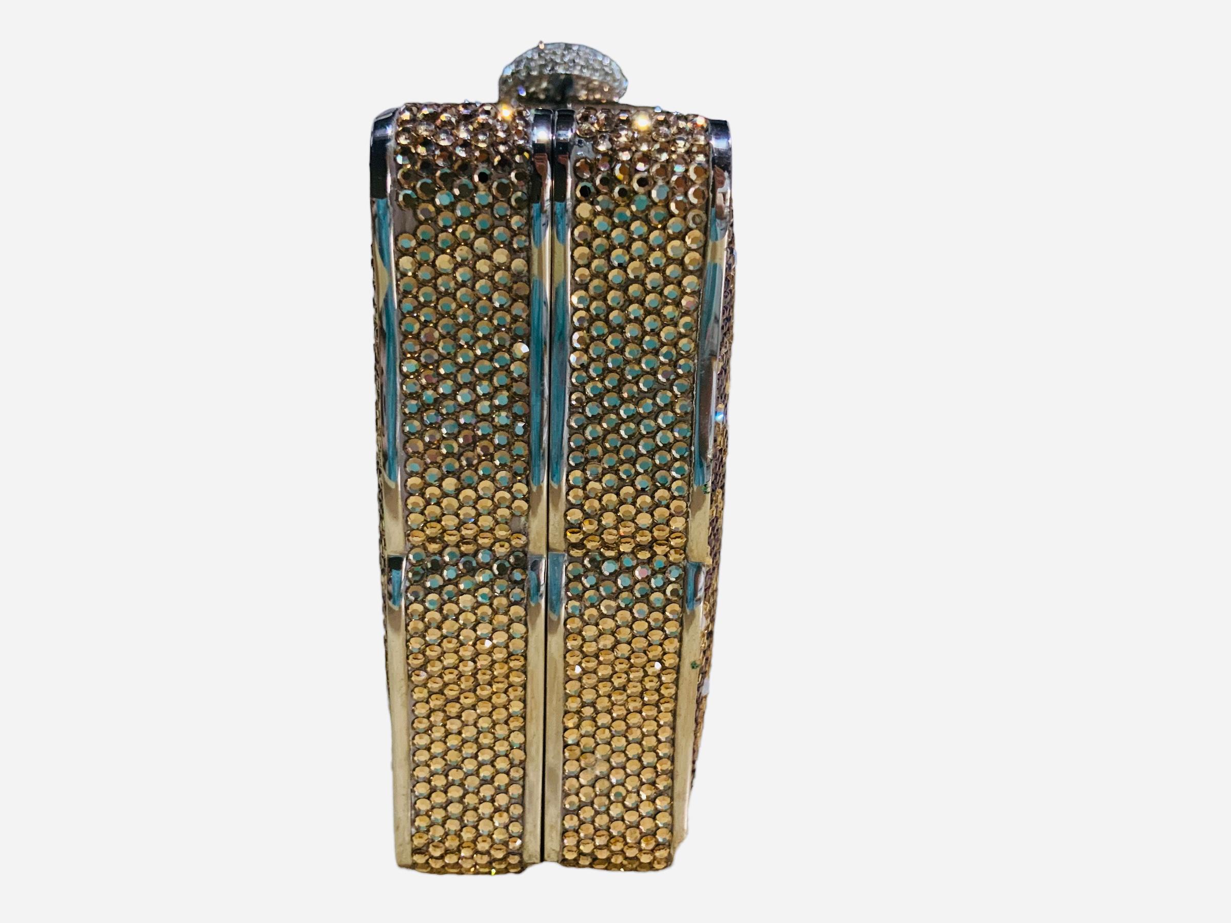 This is a Judith Leiber Swarovski Crystals Minaudiere / Clutch. It depicts a rectangular silver tone metal shaped minaudiere adorned with a large rose flower with green leaves. Large long scrolls also framed the right side of the front and back of