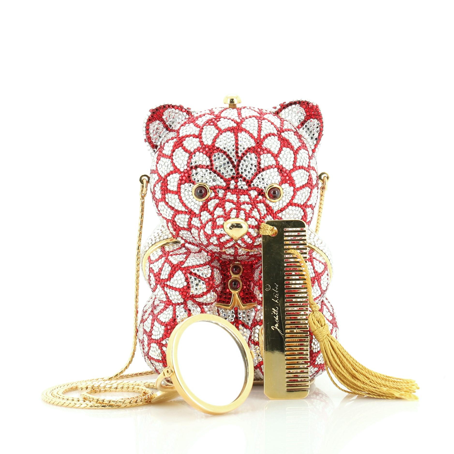 This Judith Leiber Teddy Bear Minaudiere Crystal Small, crafted from gold, red, white rhinestone, features long hidden gold chain shoulder strap, teddy bear silhouette, red crystals for the vest and gold-tone hardware. Its top-center push-lock