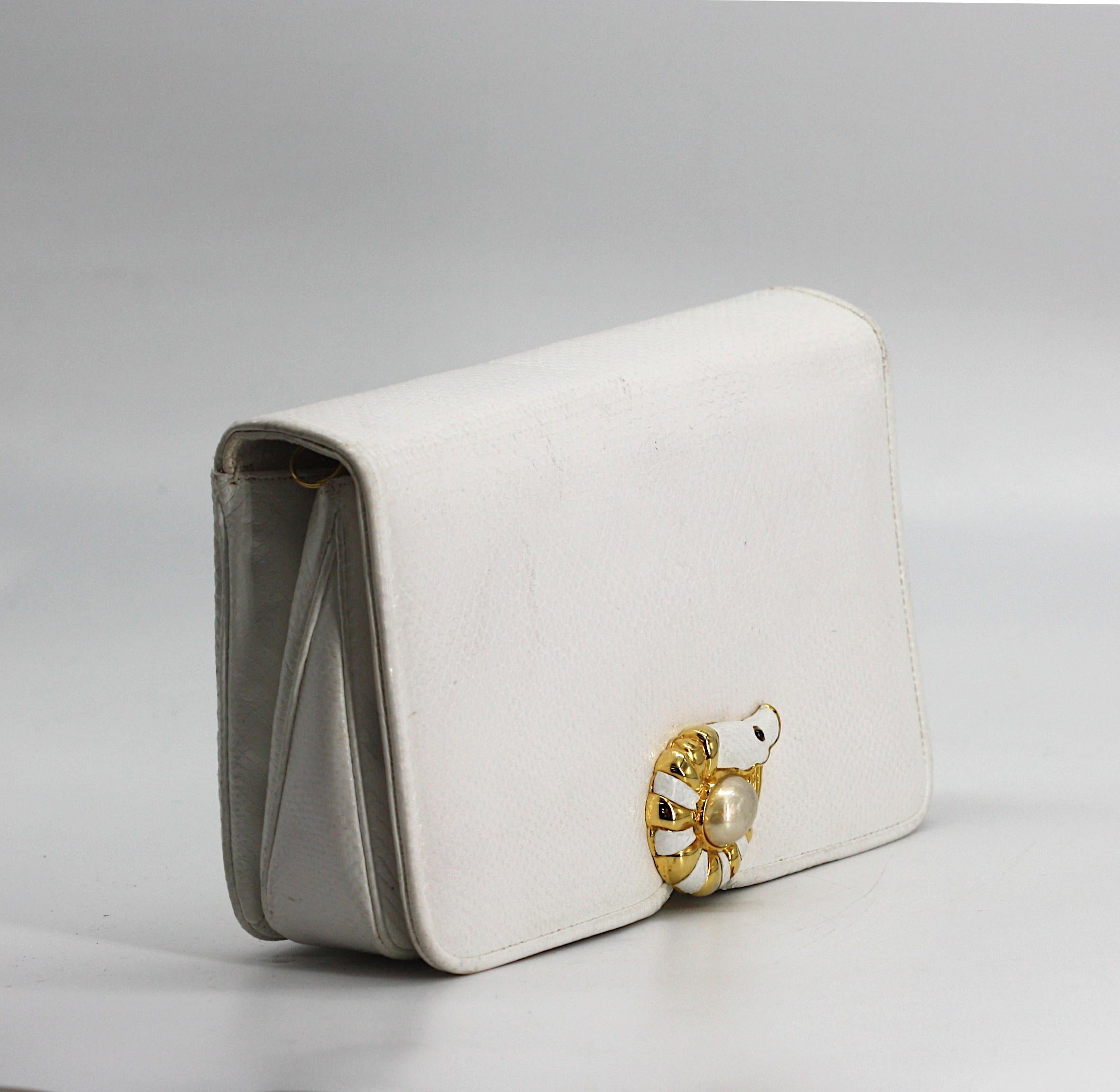 
Judith Leiber White Leather Clutch
Signed. Rectangular, with front closure flap and rear open slot, the enamel and gold toned clasp cast as a nautilus, the white fabric interior, with both an open and zippered pouch, with rings for a chain or cord,
