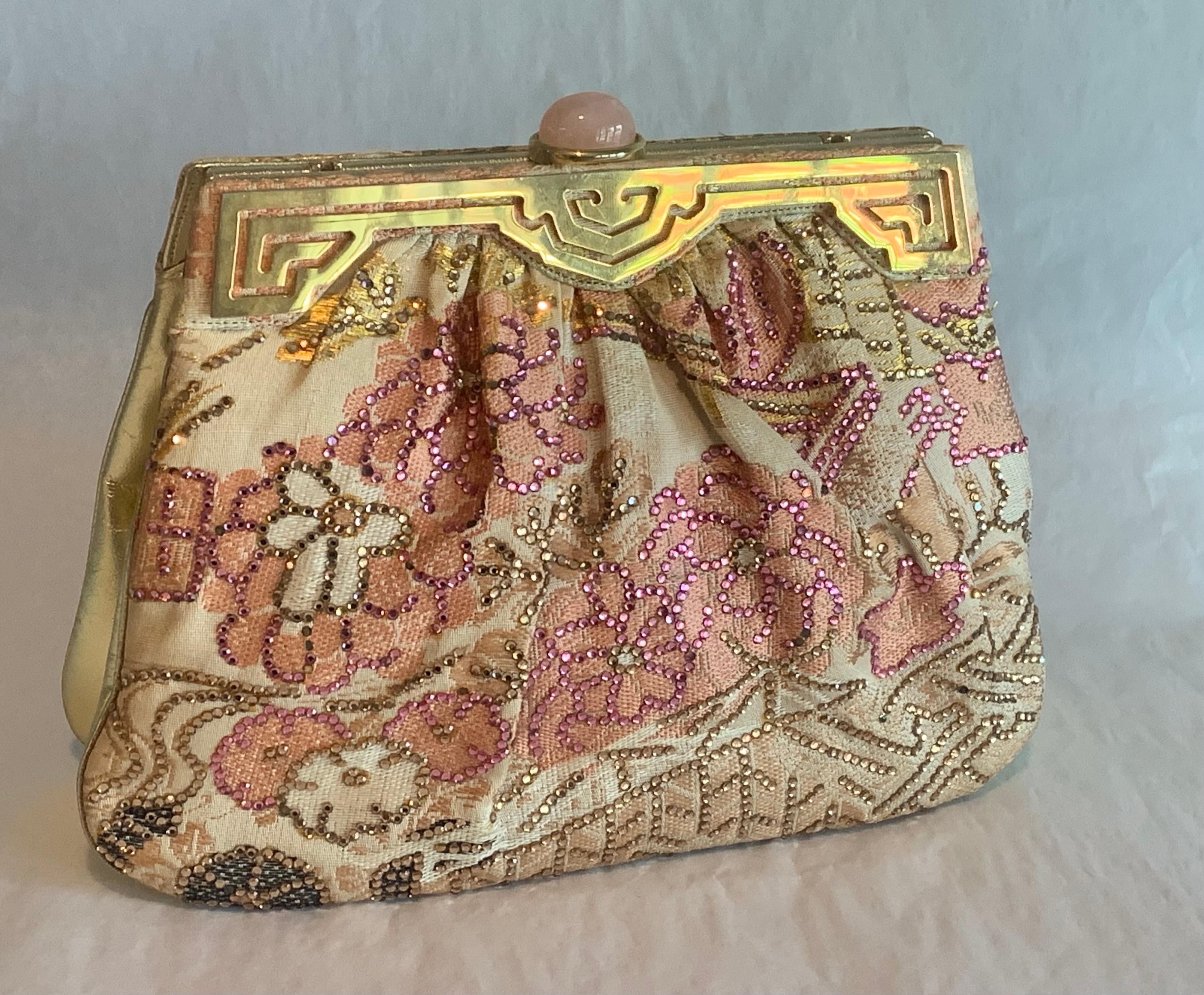 Judith Lieber has outlined the floral patten in this woven silk bag with coordinating beads in pink, gold and green. There is a gold toned frame on the front with a large pink stone as the clasp, and there is a double chain strap tucked inside. The