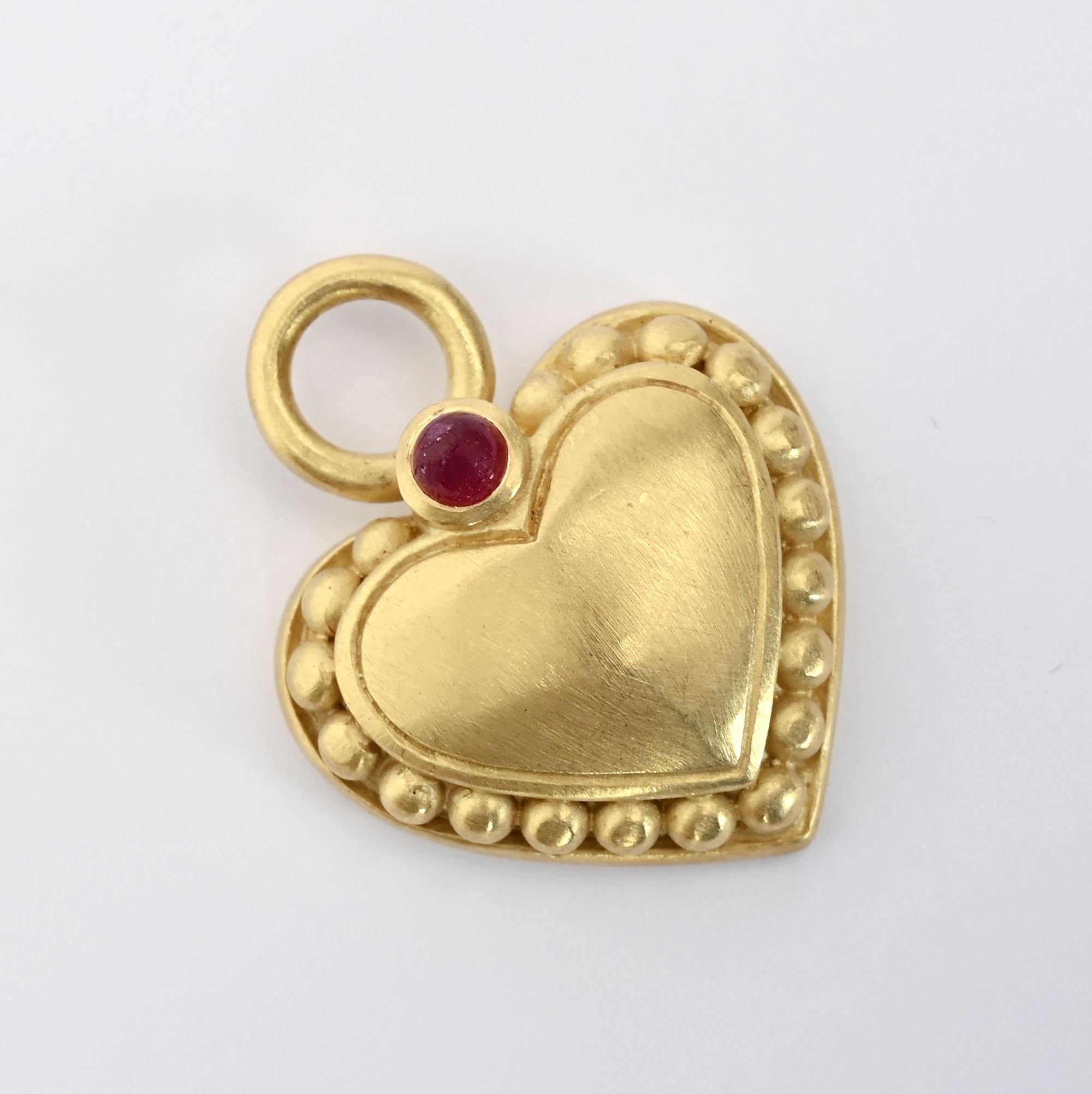 Beautifully made 18 karat gold pendant by Judith Ripka. The heart has a softly brushed finish and three dimensional balls around the interior. It is topped with a cabochon ruby. The heart measures 1 1/4 inches from top to bottom including the loop.