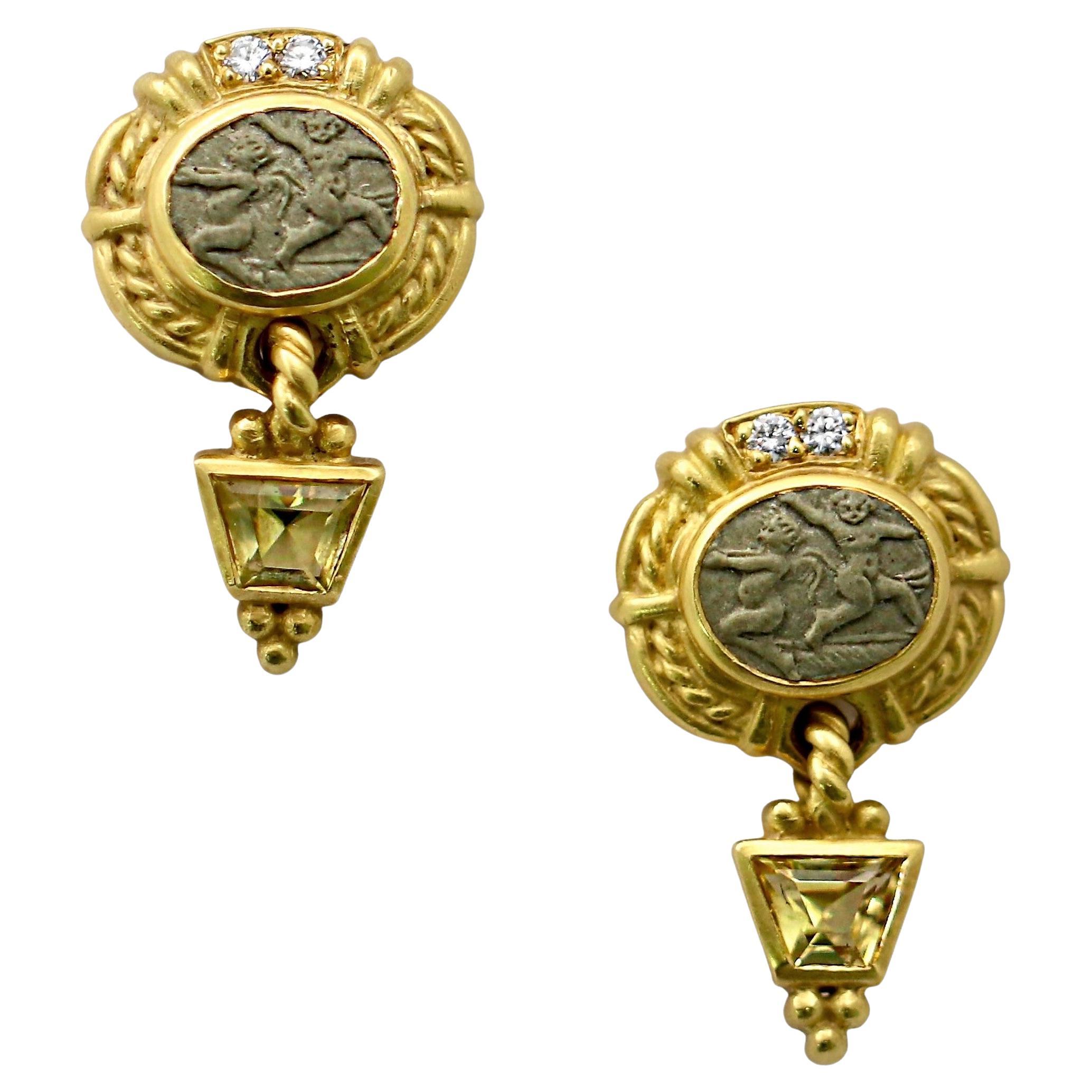 This lovely and somewhat diminutive pair of Judith Ripka 18K yellow gold dangle earrings have, as their primary design elements, oval shaped natural lava intaglios depicting putti's and cherubs. These are expertly bezel set and topped with brilliant