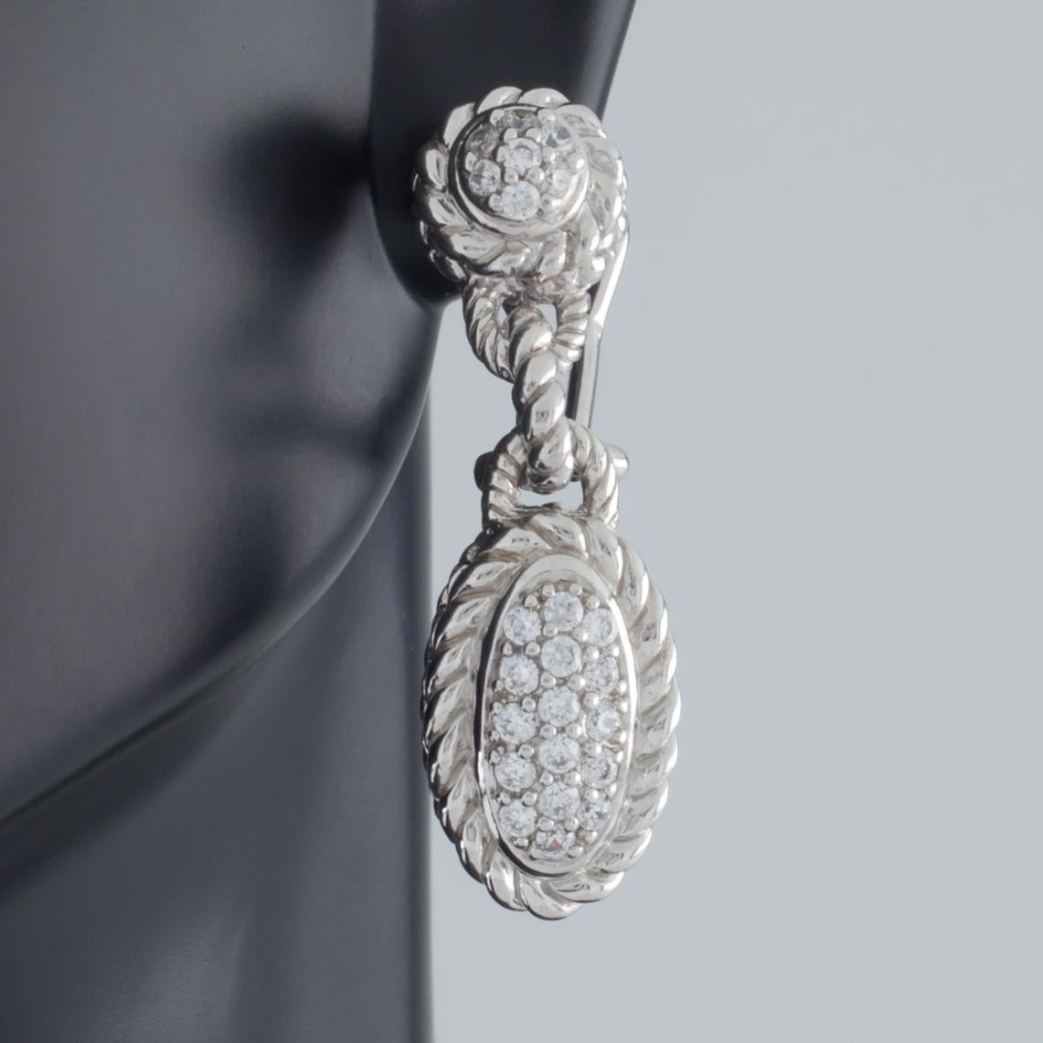 Gorgeous sterling silver earrings by Judith Ripka.
Feature textured, dangling oval silver plaques set with cubic zirconia.
Omega backs with posts.
Drop Length: 34 mm.
Width: 10 mm.
Metal: 0.925 sterling silver.
Weight: 12.8 grams.