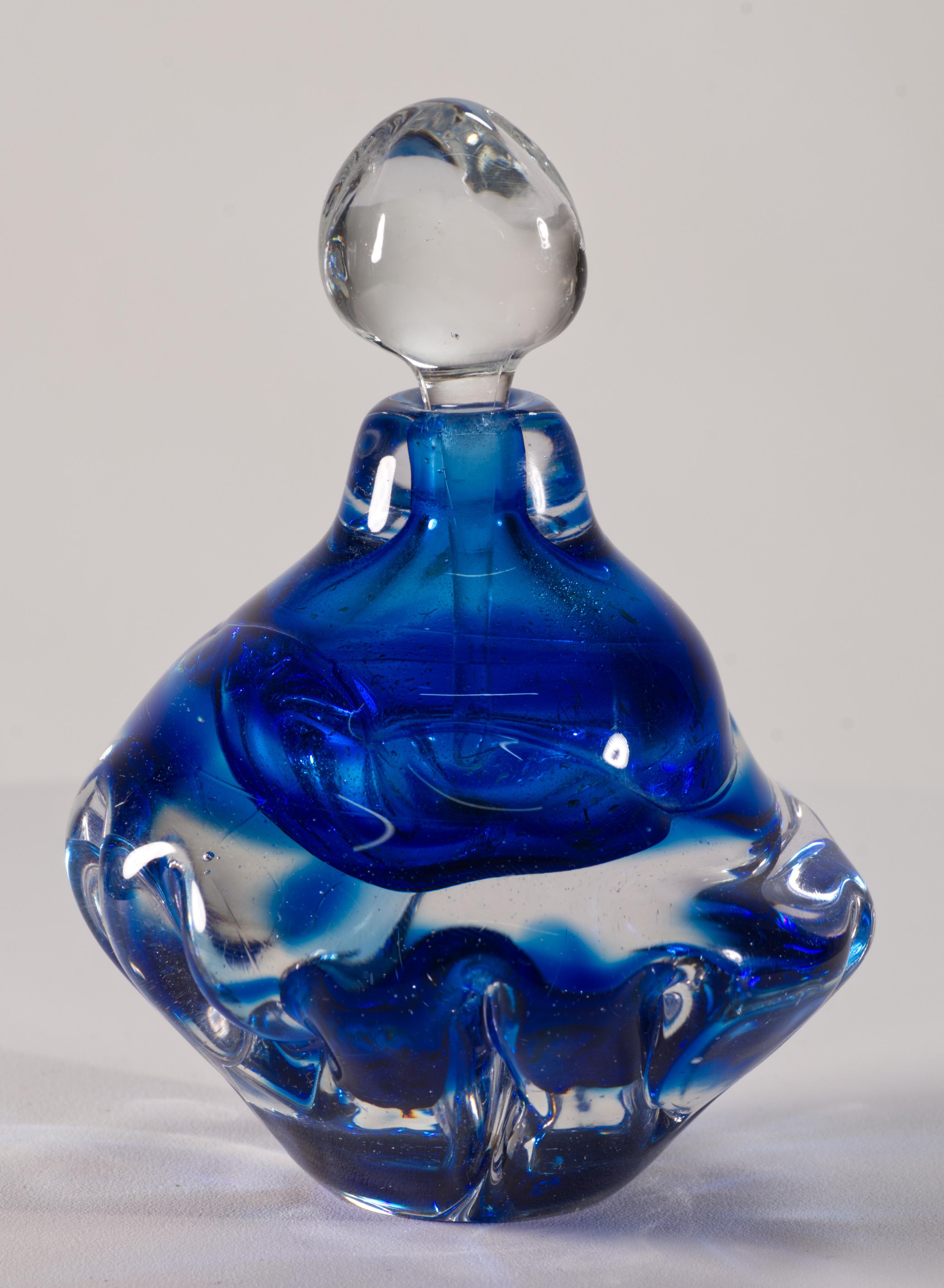  Il flacone di profumo in vetro artistico d'epoca è stato soffiato a mano con la tecnica del sommerso, con un gruppo di vetro blu cobalto dai colori gioiello racchiuso in vetro trasparente; la forma organica e moderna del flacone continua fino al